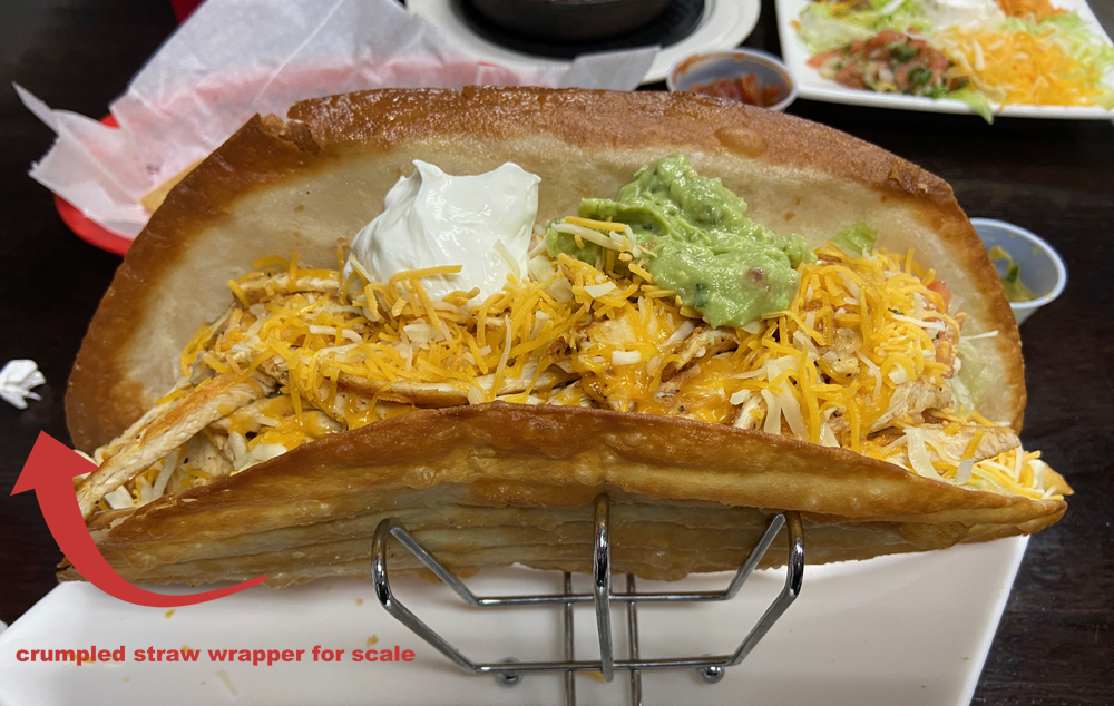 Photo of a foot long, fried taco with chicken and cheese, sour cream, and guacmole. There is a graphic arrow pointing to a crumpled straw wrapper and text that reads 