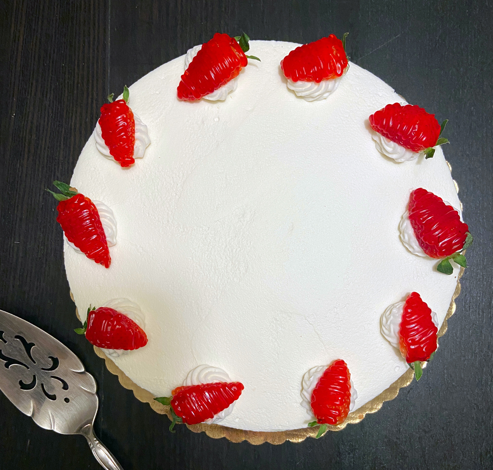 Photo of a round cake with white whipped cream frosting and strawberries around the edge. Photo by Jessica Hammie.