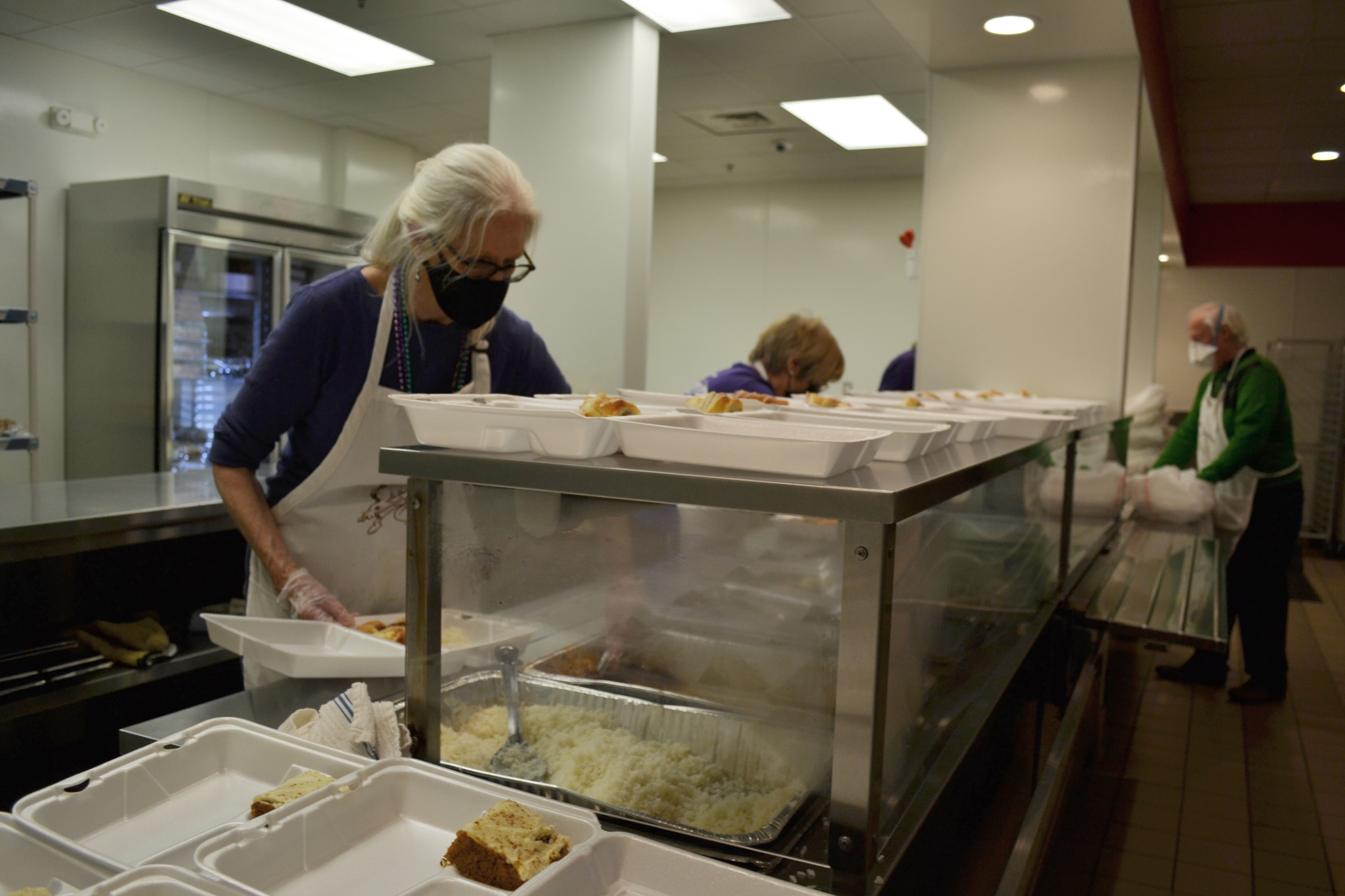Volunteers are masked and serving up portions into white clamshell containers for to go meals. Photo by Alyssa Buckley.