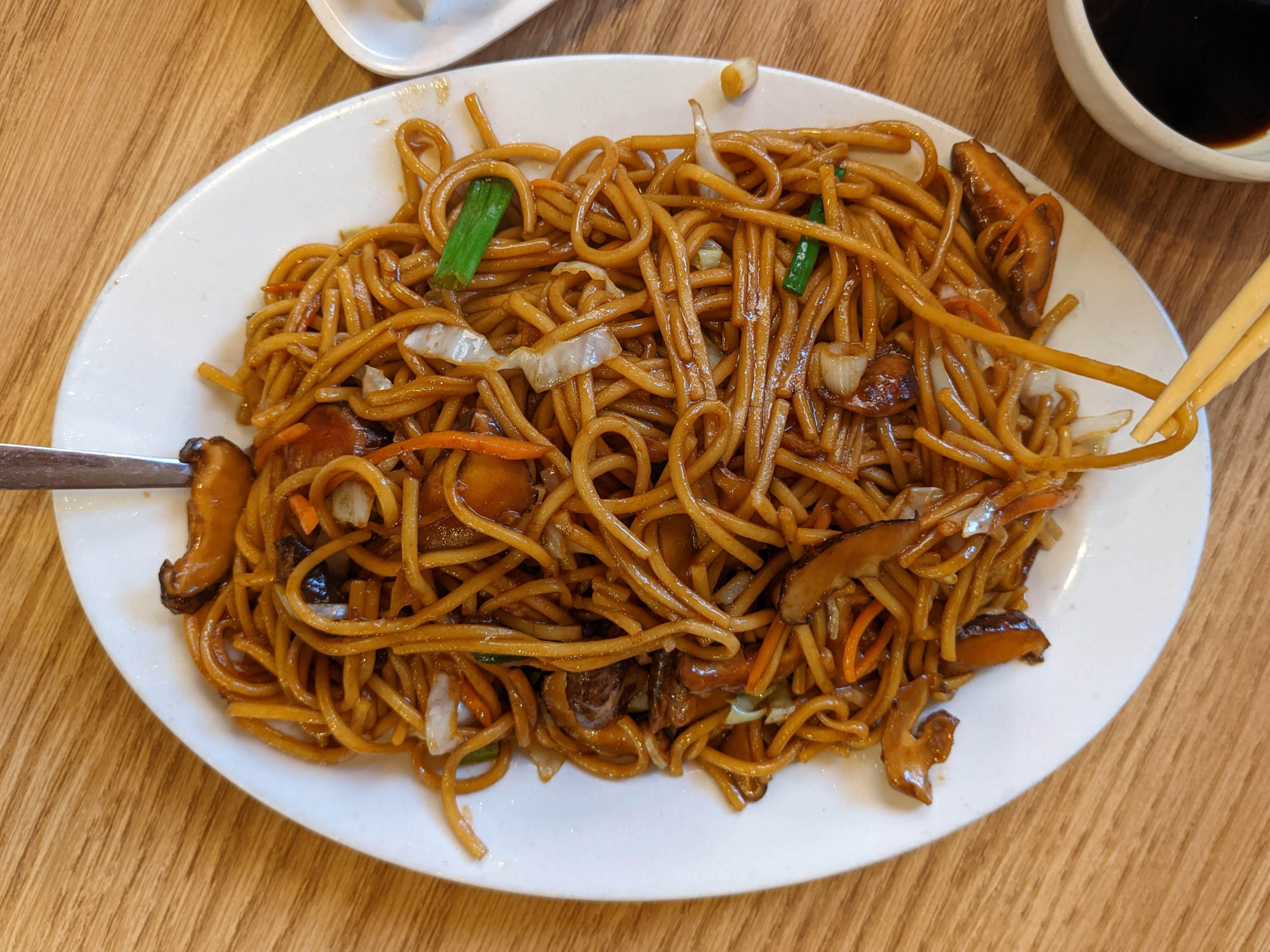On a wooden table, there is a white plate full of mushroom chow mein. Photo by Tayler Neumann.