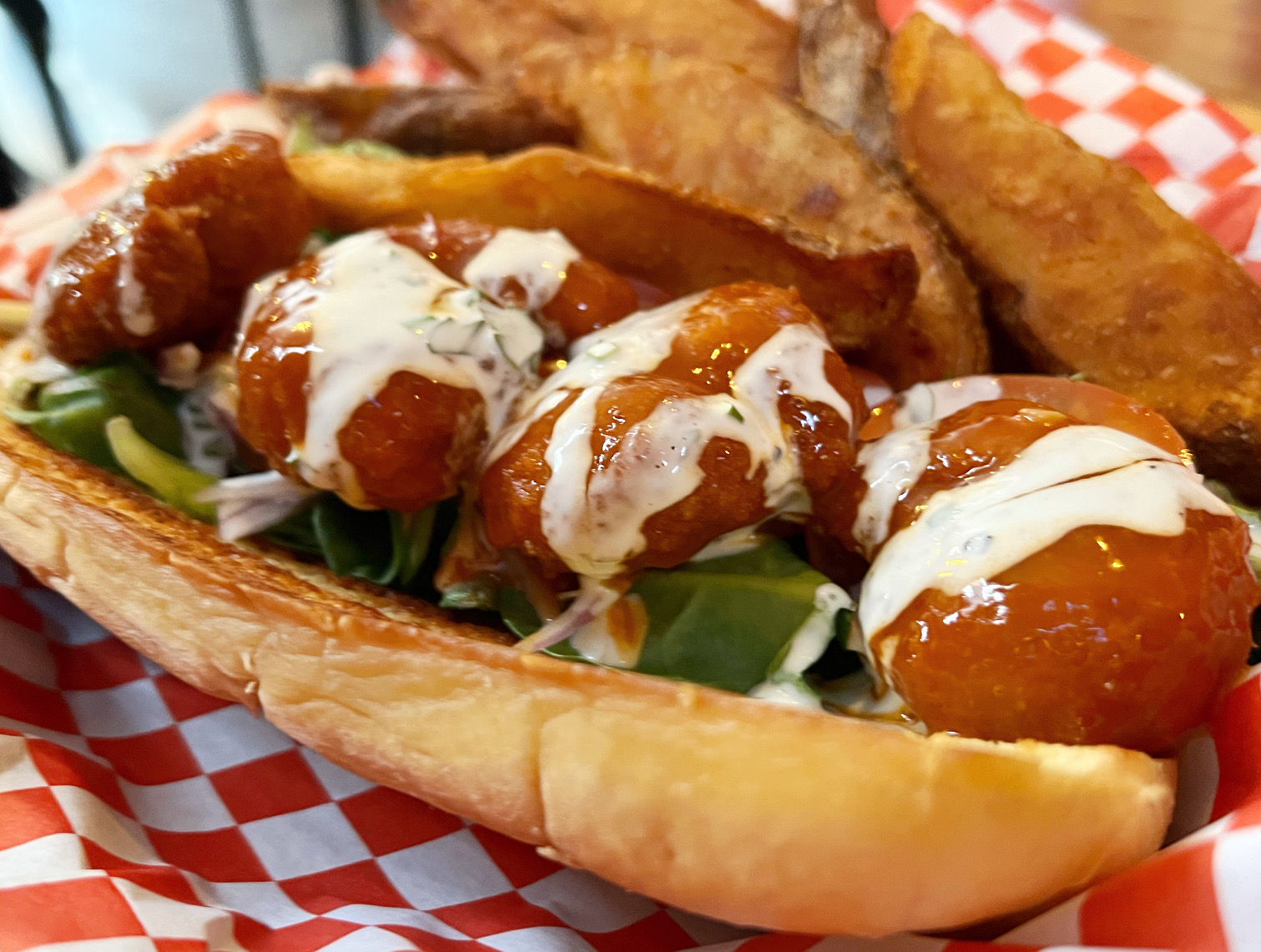 A close up of the firecracker shrimp po boy shows fried shrimp covered in an orange sauce drizzled with a white sauce. Photo by Alyssa Buckley.