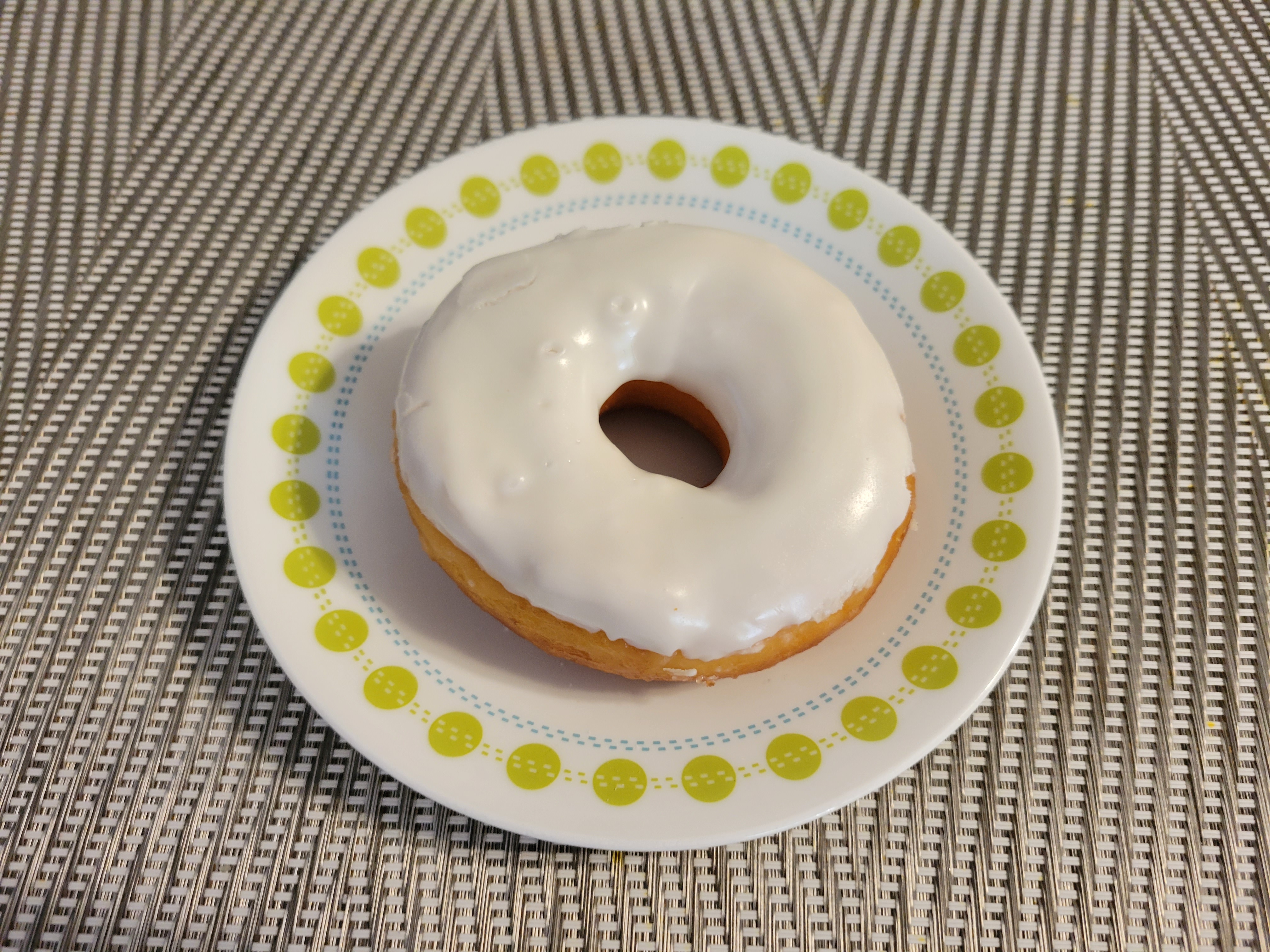 On a gute placemat, there is a white plate with a vanilla frosted yeast donut. Photo by Matthew Macomber.