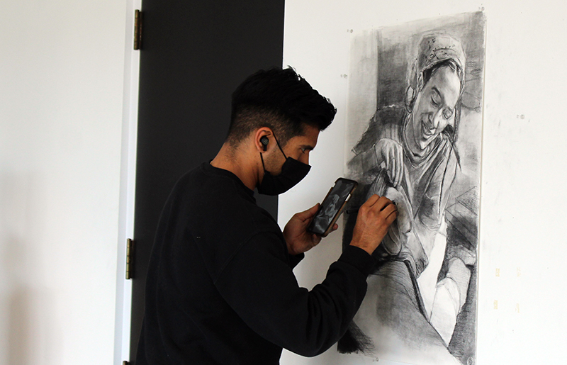 Photo of artist Chris Marin sketching in charcoal with image of woman almost completed.