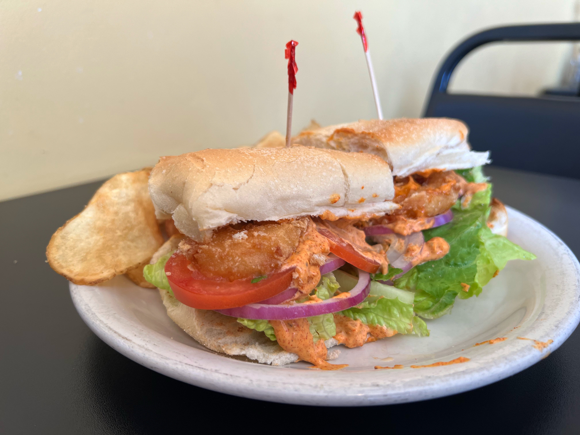 On a white plate, there is a sandwich with an orange sauce and toppings falling out of it. There are two toothpicks, one in each side of the sandwich. Photo by Alyssa Buckley.