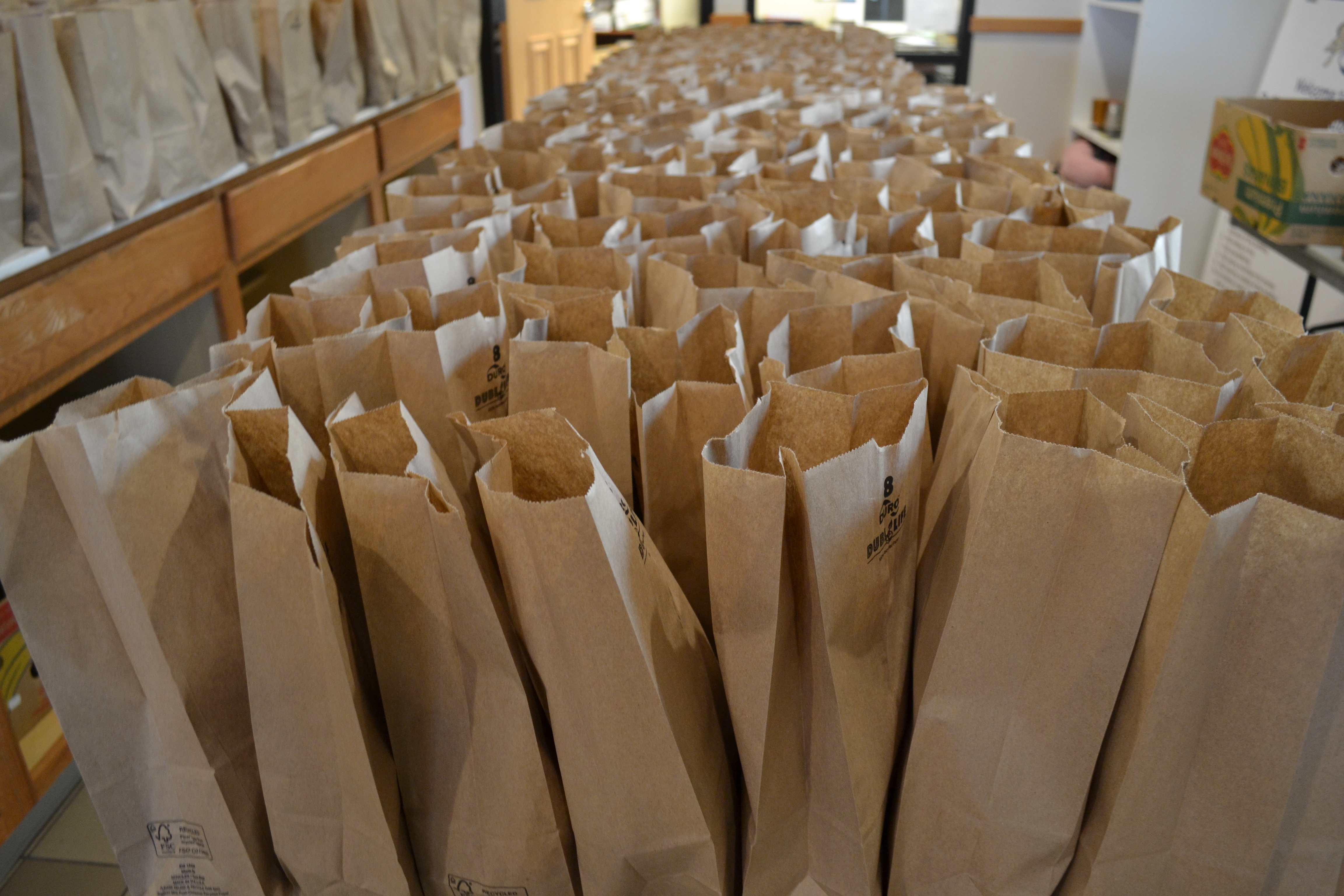 On a table, hundreds of brown bags are ready for distribution. Photo by Alyssa Buckley.