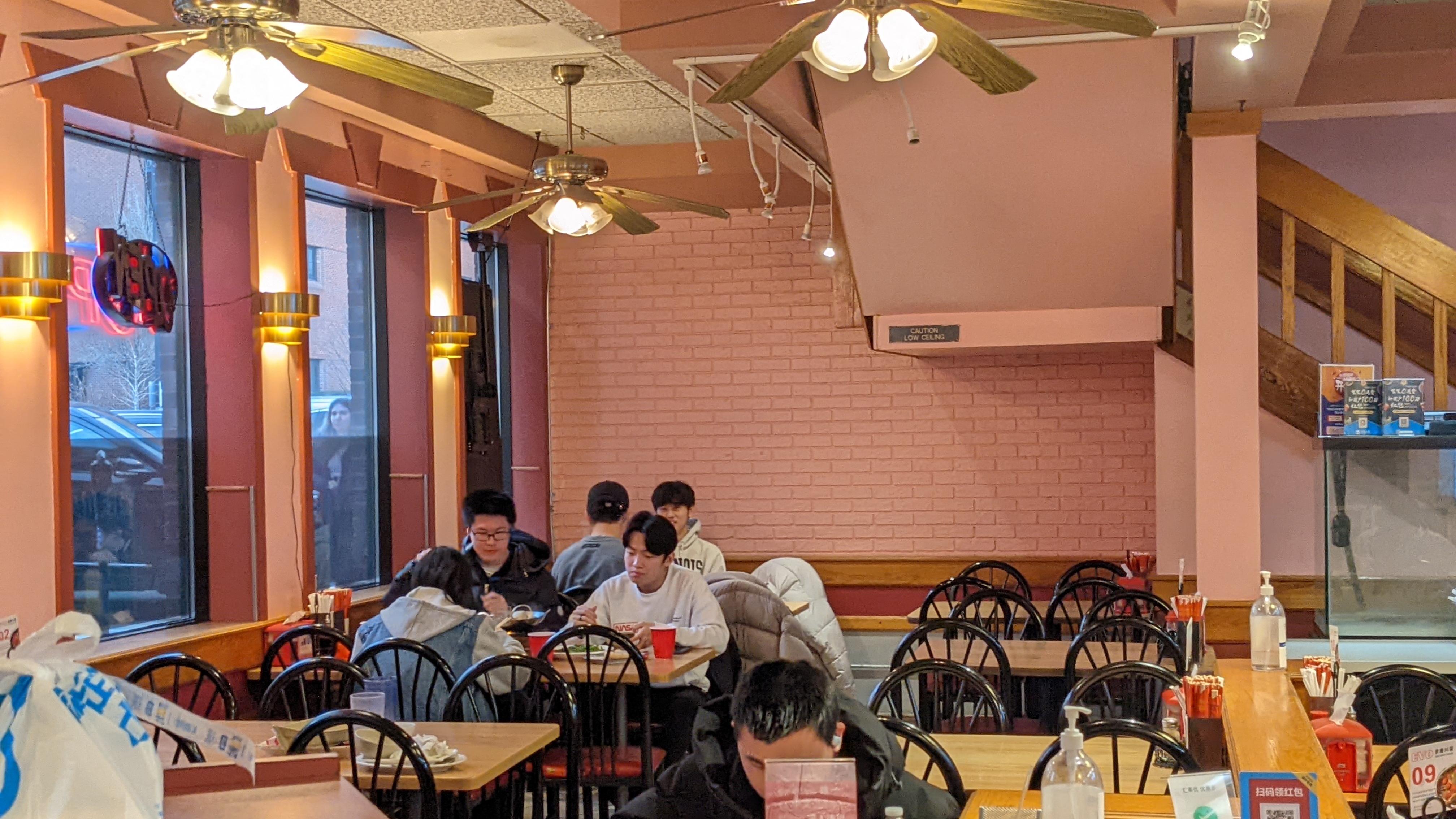 Inside Evo Cafe, there are diners seated at tables with black metal chairs. The brick walls are painted light pink, and the overhead ceiling fans are traditional style and lit. Photo by Tayler Neumann.