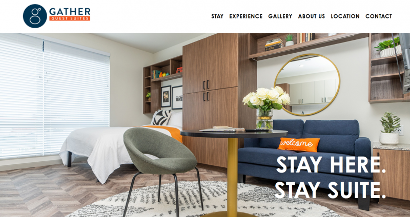Screenshot from a website. There is a photo of a room with a bed, couch, chair and table, and armoire. There is a large window with with white shades. Screenshot from Gather website.