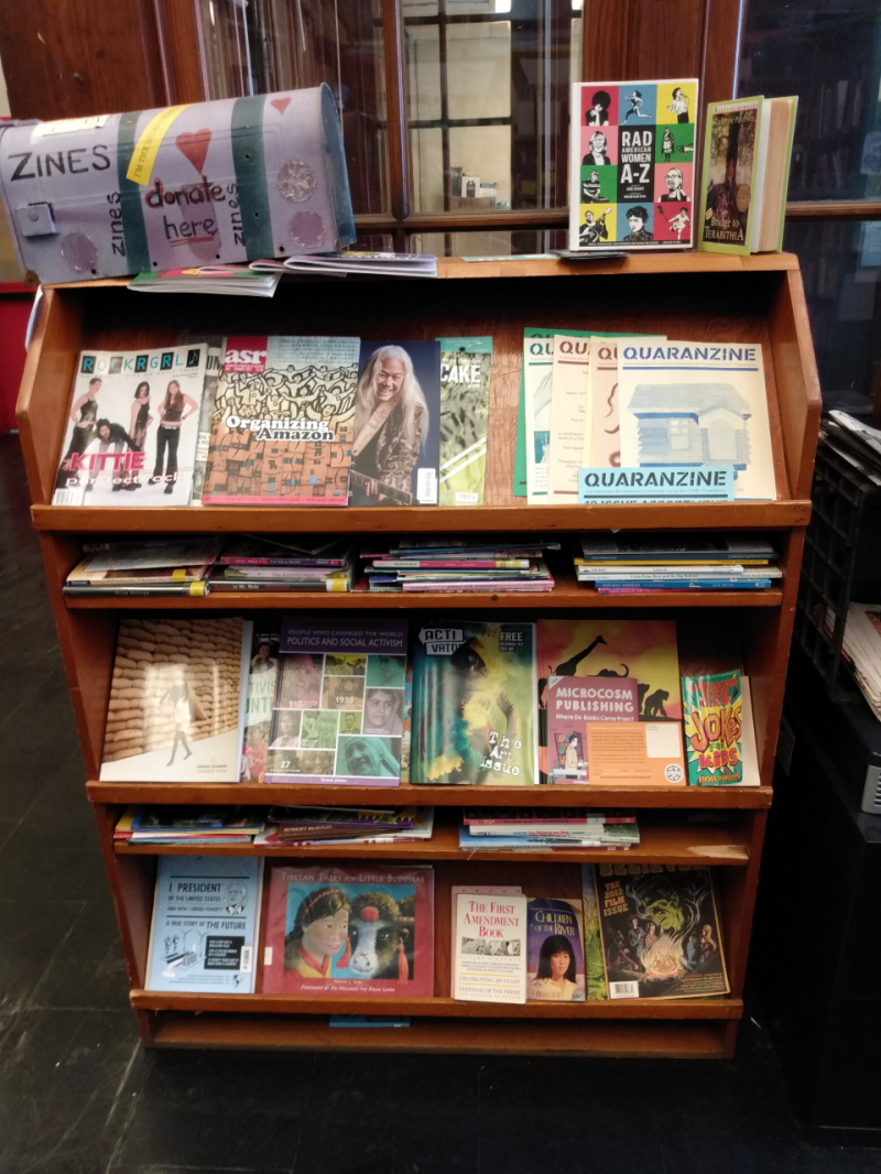 A shelf in the Independent Media Center displaying current publications, such as the magazines Activator and Jacobin alongside other small and independent publications. On the top left is a mailbox painted purple where the IMC accepts donations for the Zine Library. Photo by Michael O'Boyle.