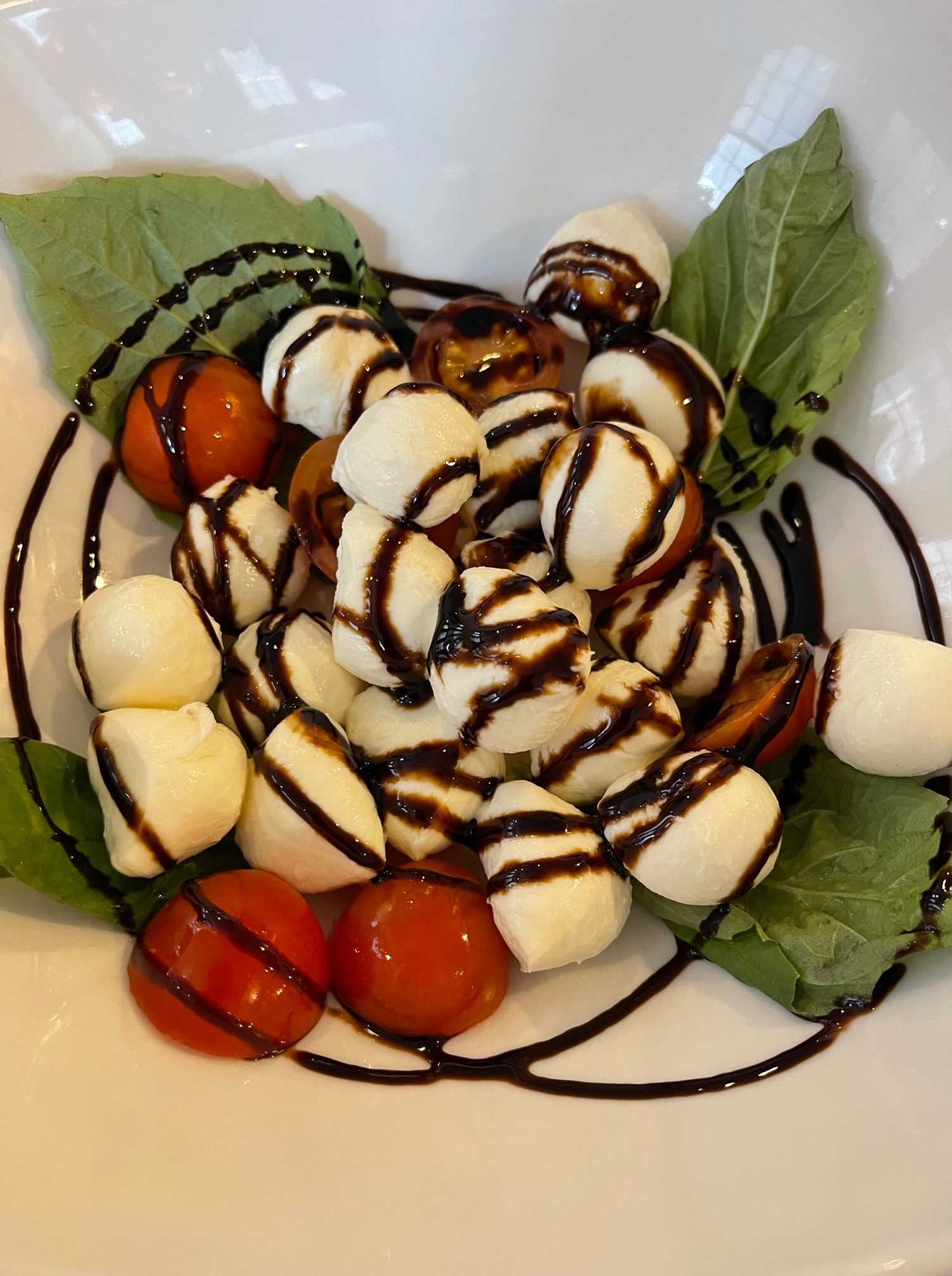 On a white plate, there is a Caprese salad with red tomatoes, mini balls of mozz, and a thick pretty drizzle of balsamic. Photo by Stephanie Wheatley.