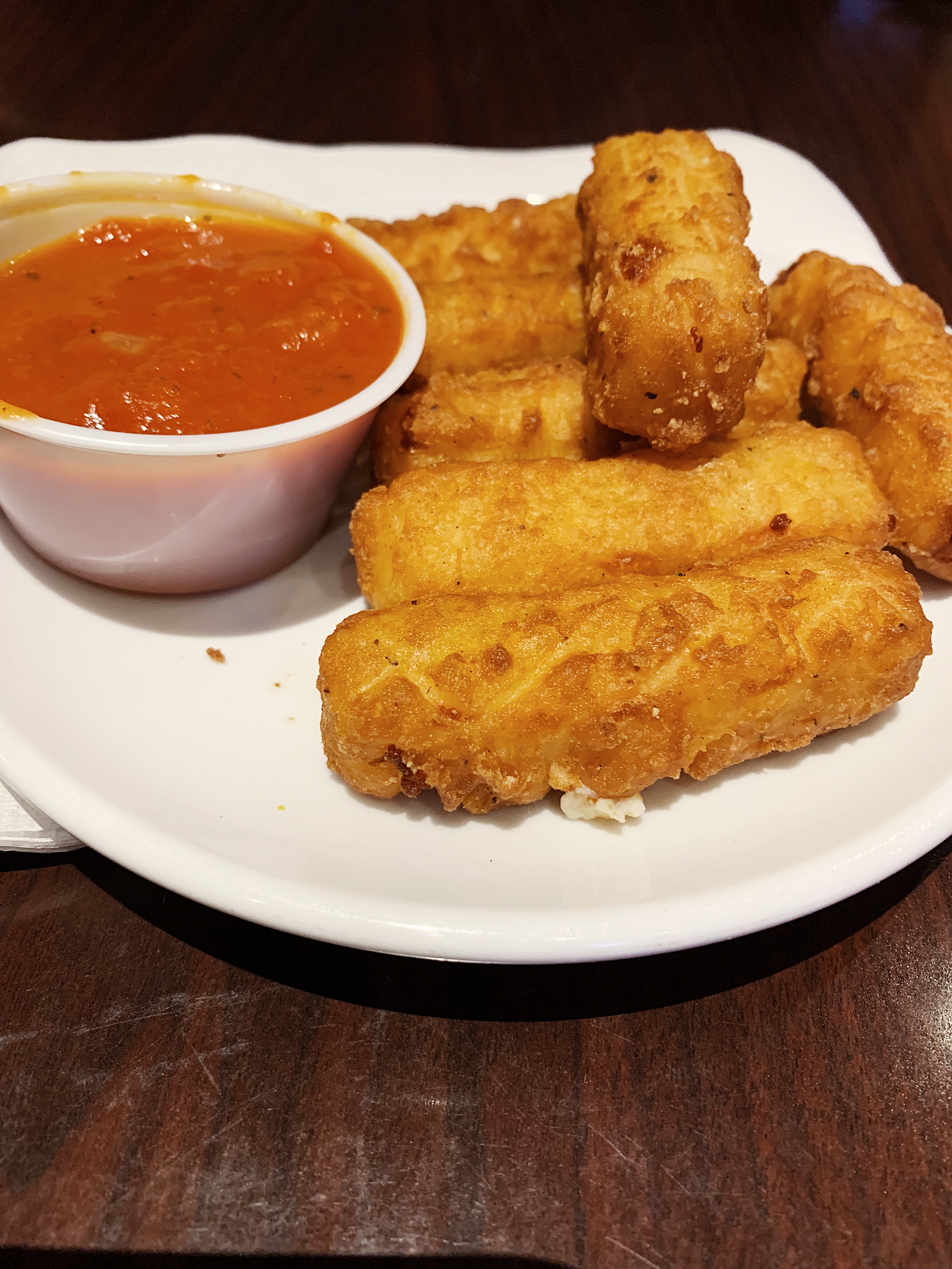 On a white plate, there are fried cheese sticks beside a cup of marinara. Photo by Anya Uppal.