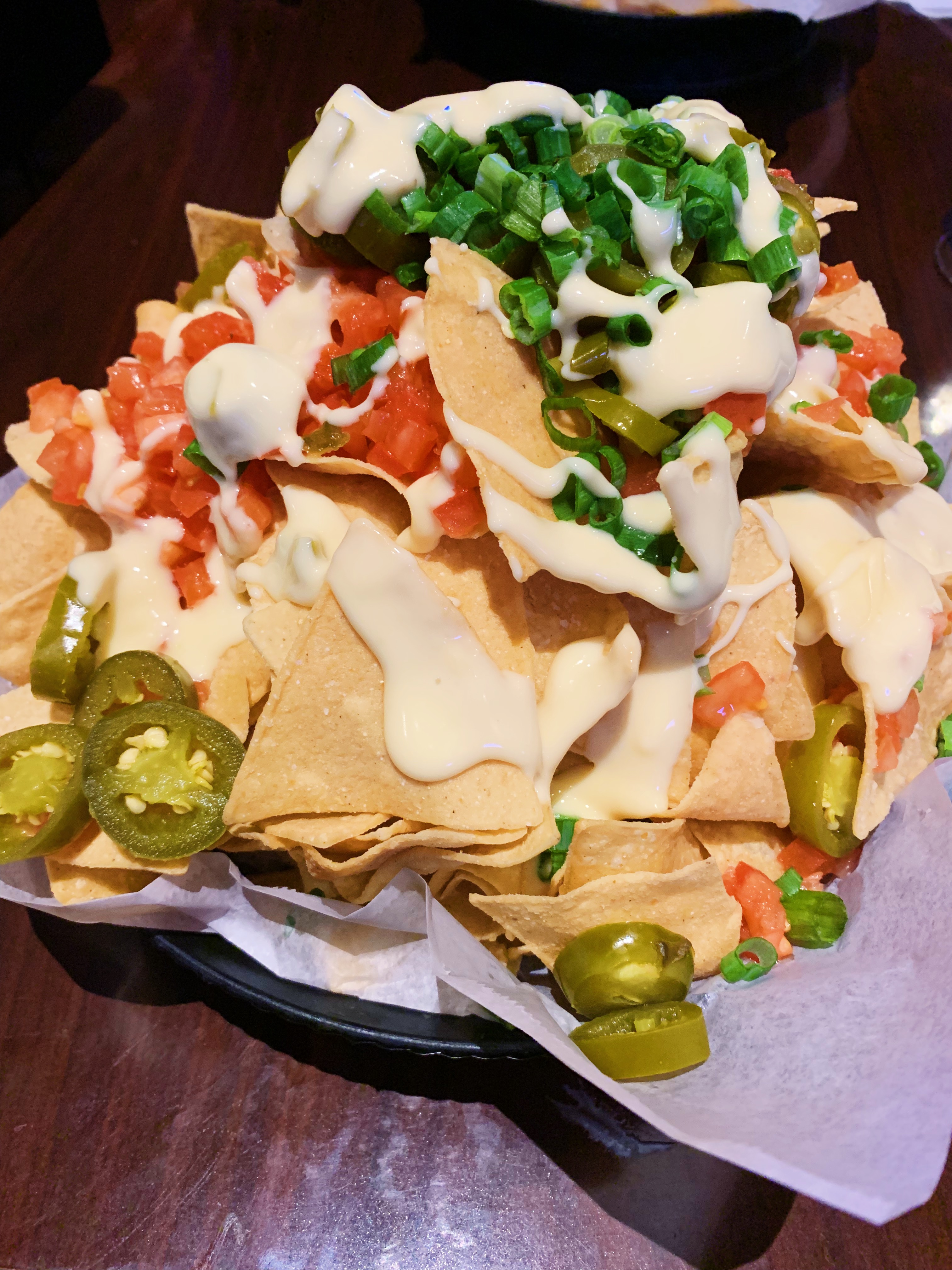 On a brown table, there is a pile of nachos from Billy Barooz. There is cheese, tomatoes, jalapeno, and toppings on many chips. Photo by Anya Uppal.