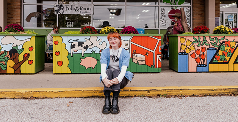 Photo of artist Madeline Witruck in front of her grant sponsored mural in front of the Common Ground Food Coop.