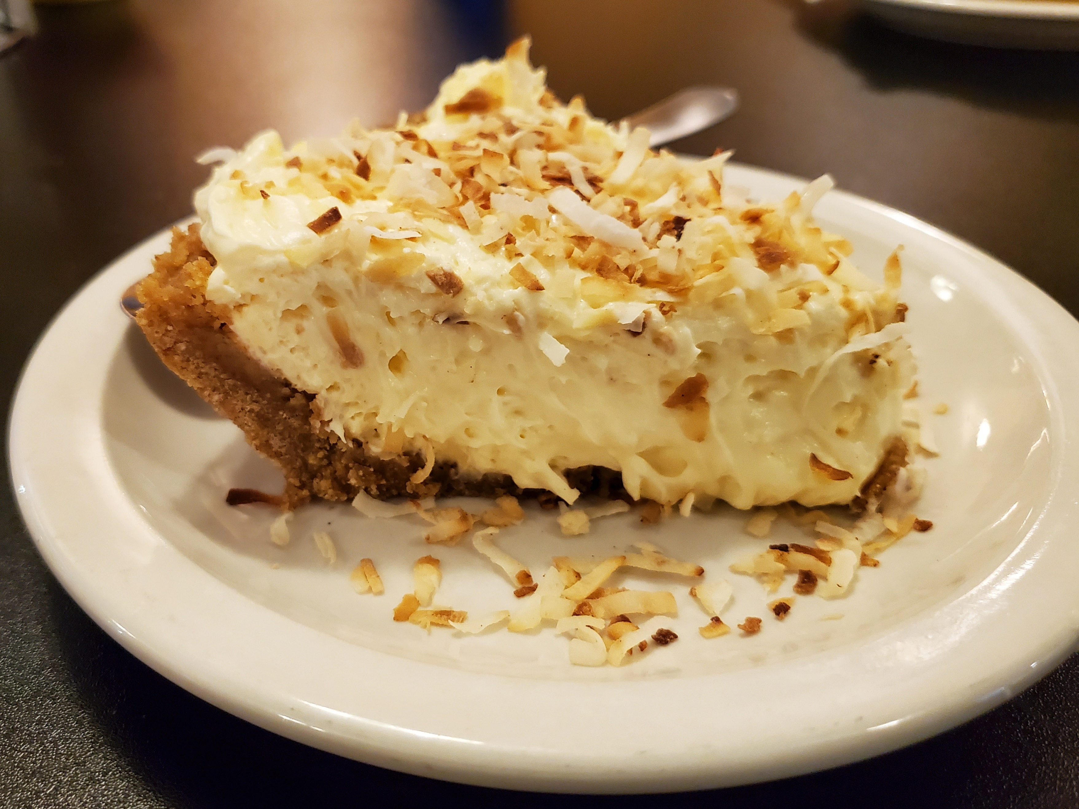 On a white plate, there is a slice of coconut cream pie with toasted coconut shavings. Photo by Carl Busch.