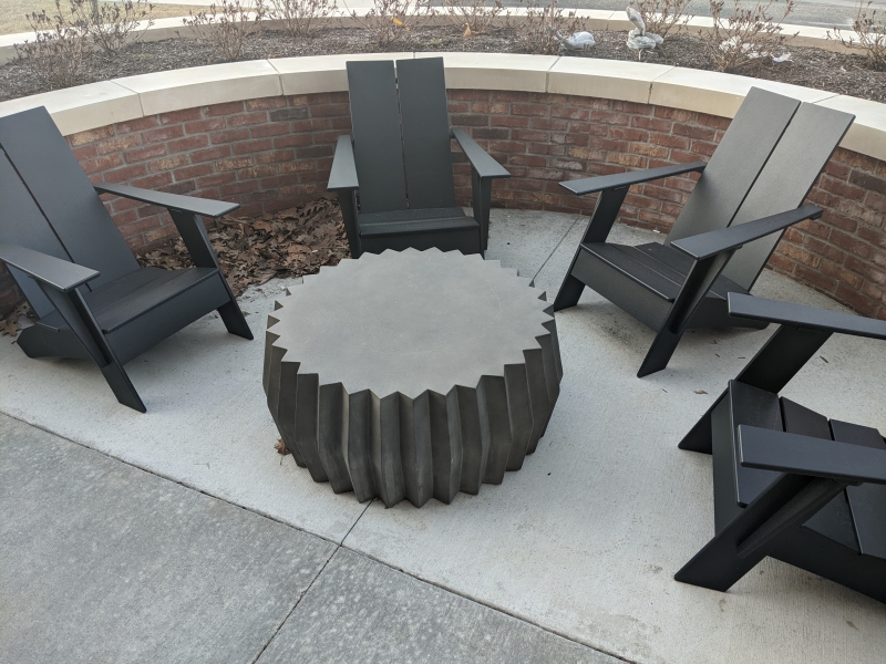 Four black Adirondack chairs are in a semi-circle on a concrete patio. There is a round table in the center that has ridges around the outside. Photo by Tom Ackerman.