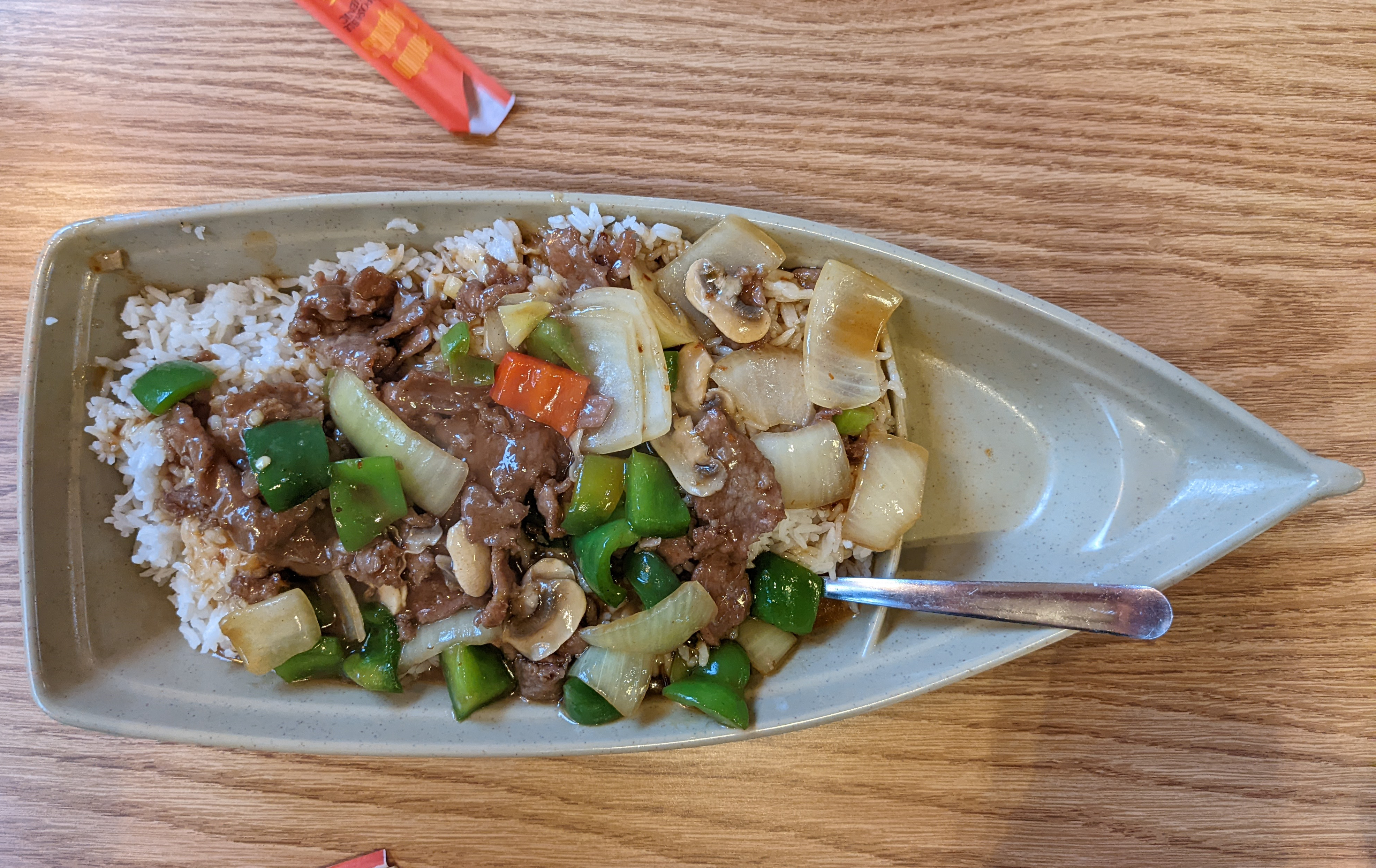 In a gray porcelain boat, there is a beef dish over rice with veggies. Photo by Tayler Neumann.