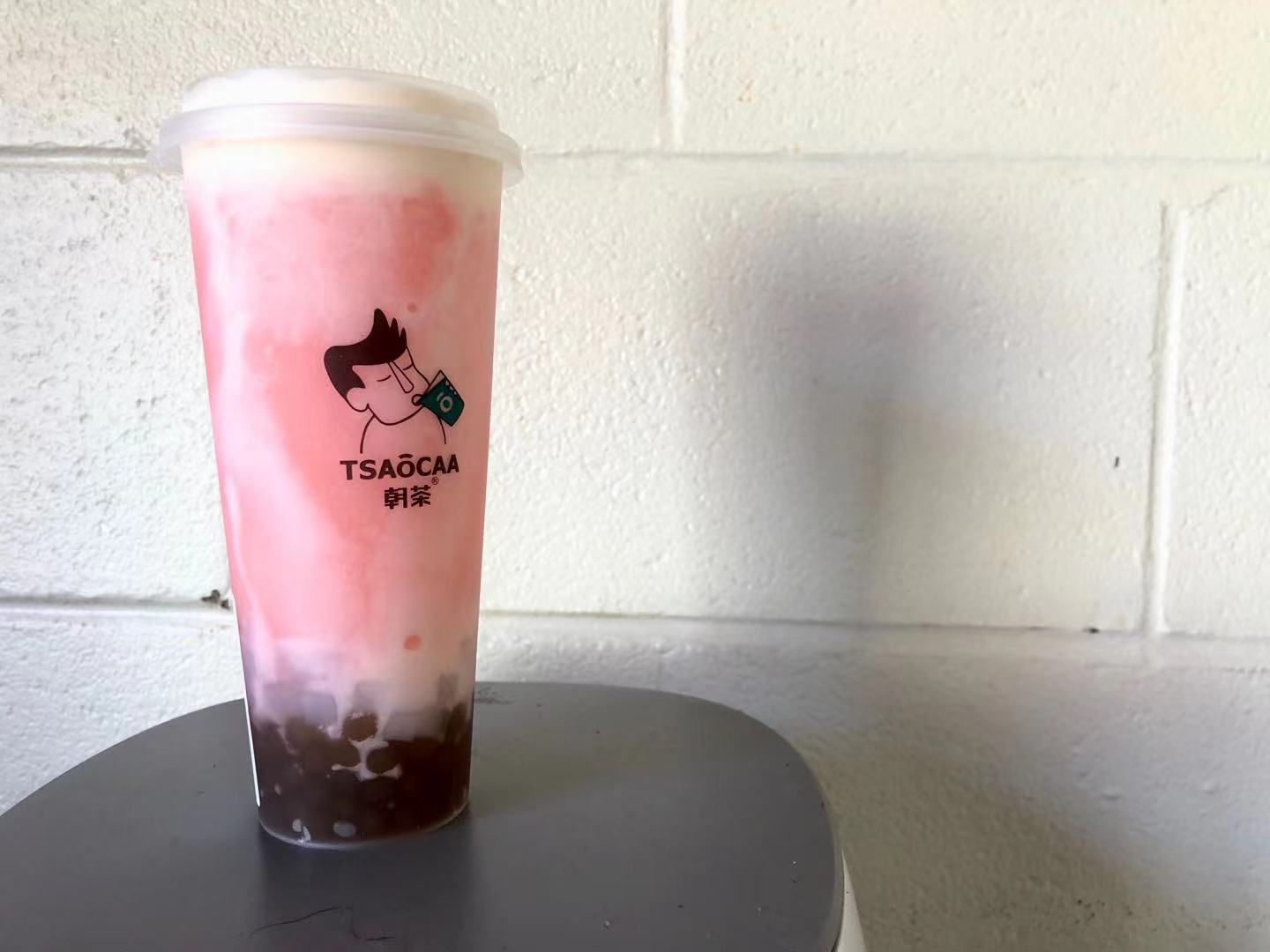 On a black circular table, there is a pink boba drink in a plastic cup that reads: Tsaoom. Photo by Xiaohui Zhang.