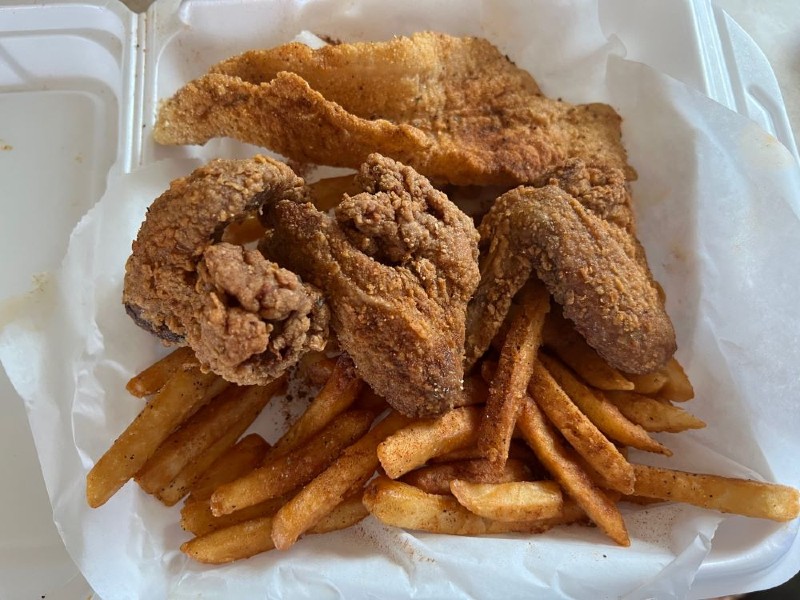 In a styrofoam takeout container, there are pieces of fried chicken and fried fish over a bed of fries from Da Shark in Champaign. Photo by Julie McClure.