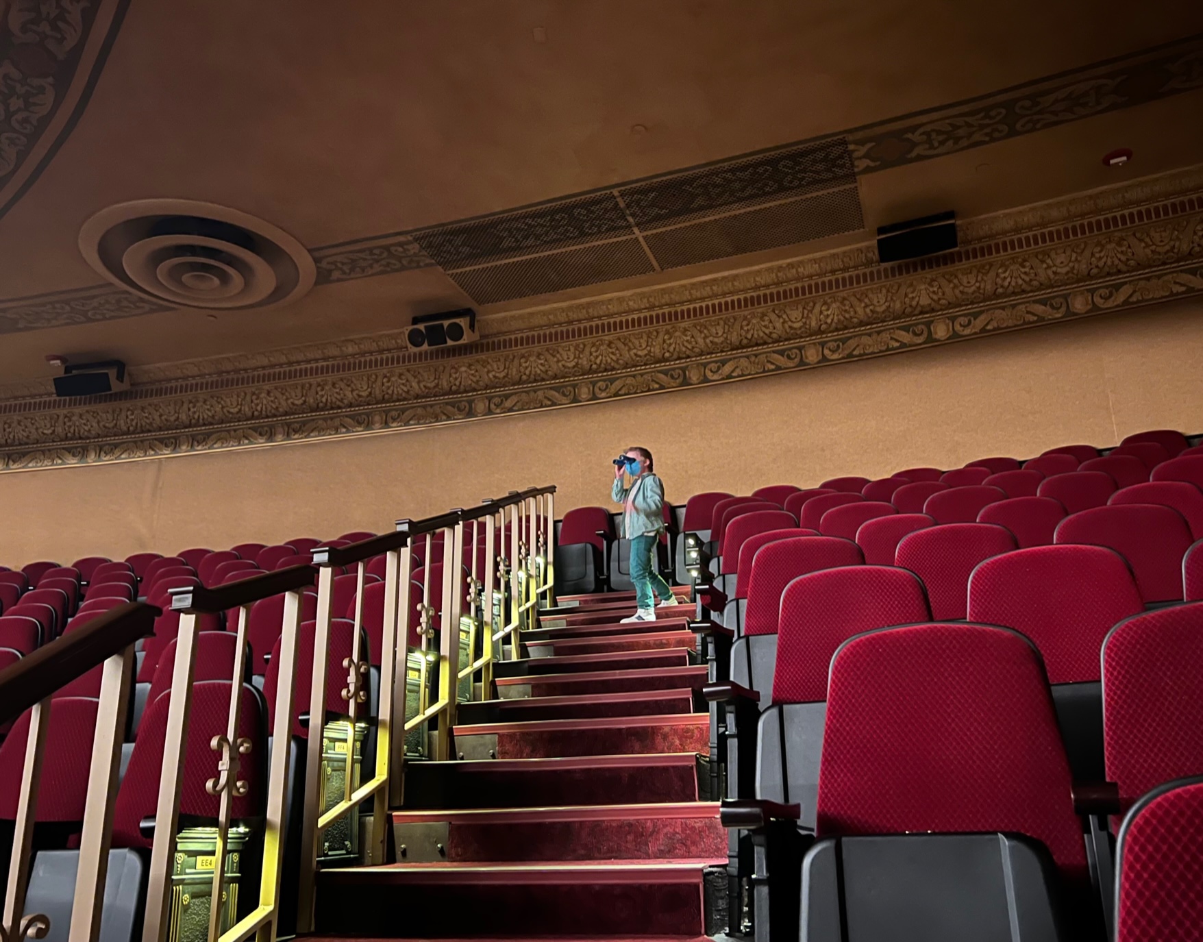 In the Virginia Theatre, a small child holds binoculars to his eyes to see the stage from the back row. Photo by Alyssa Buckley.