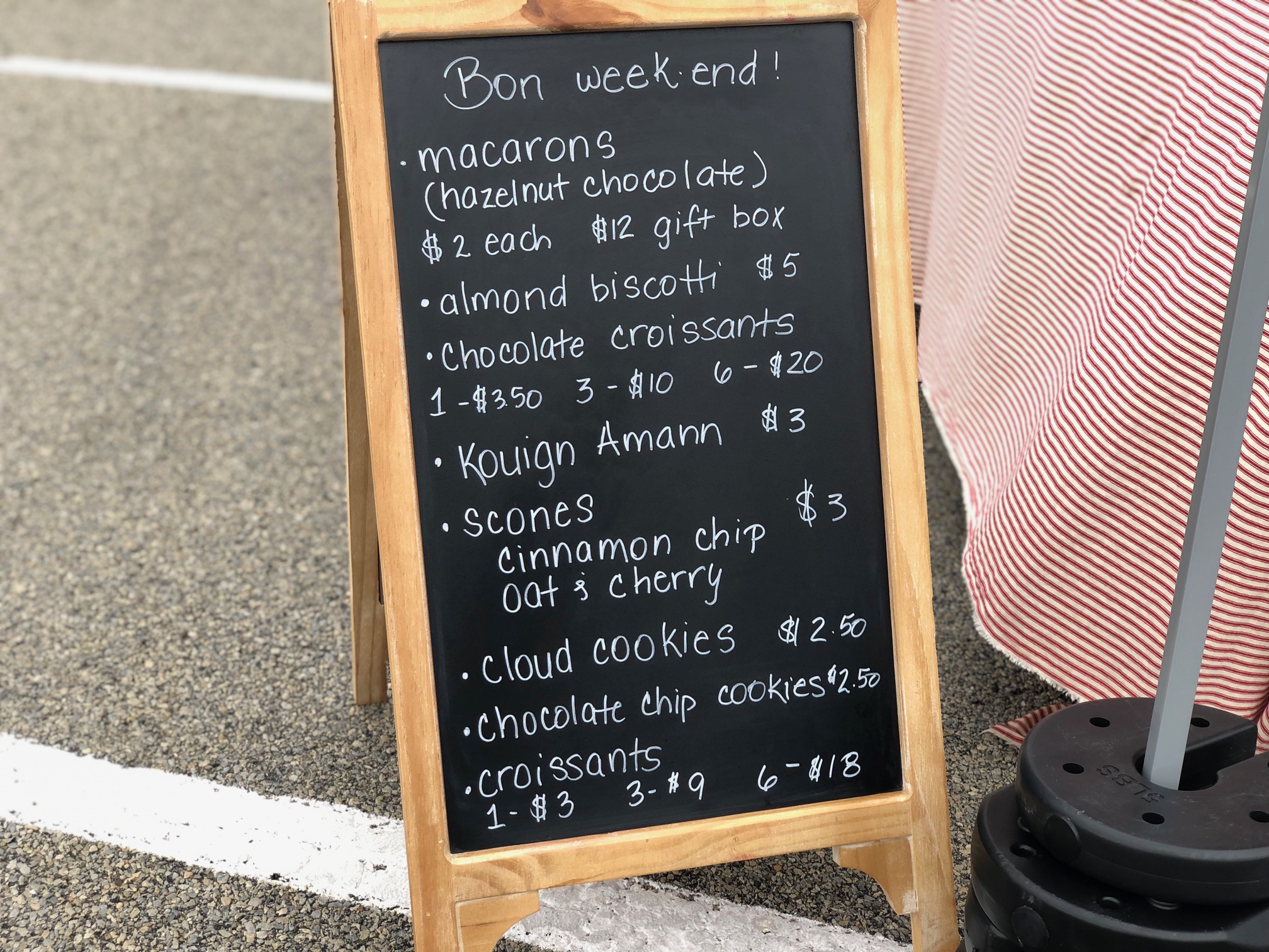 In the parking lot at the Urbana Market at the Square, there is a chalkboard sign with the names of baked goods and prices written neatly with white chalk.  Photo by Alyssa Buckley.