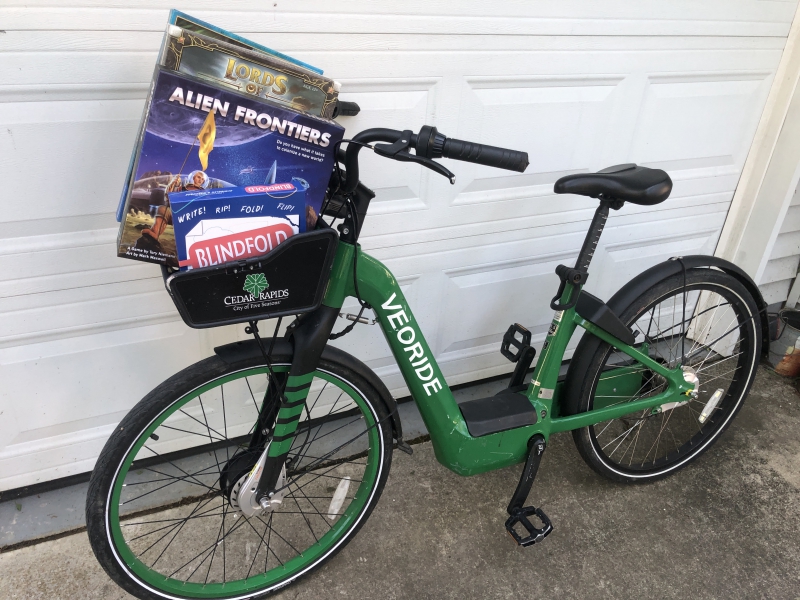 The green veoride bike has several game boxes lined up in the black basket. Photo by Andrea Black.