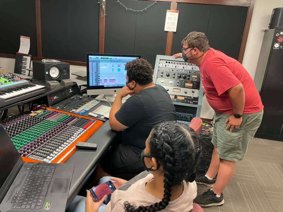 Three students work in front of a large sound mixing board, in the studio at Perimeter Road Sound Recordings.