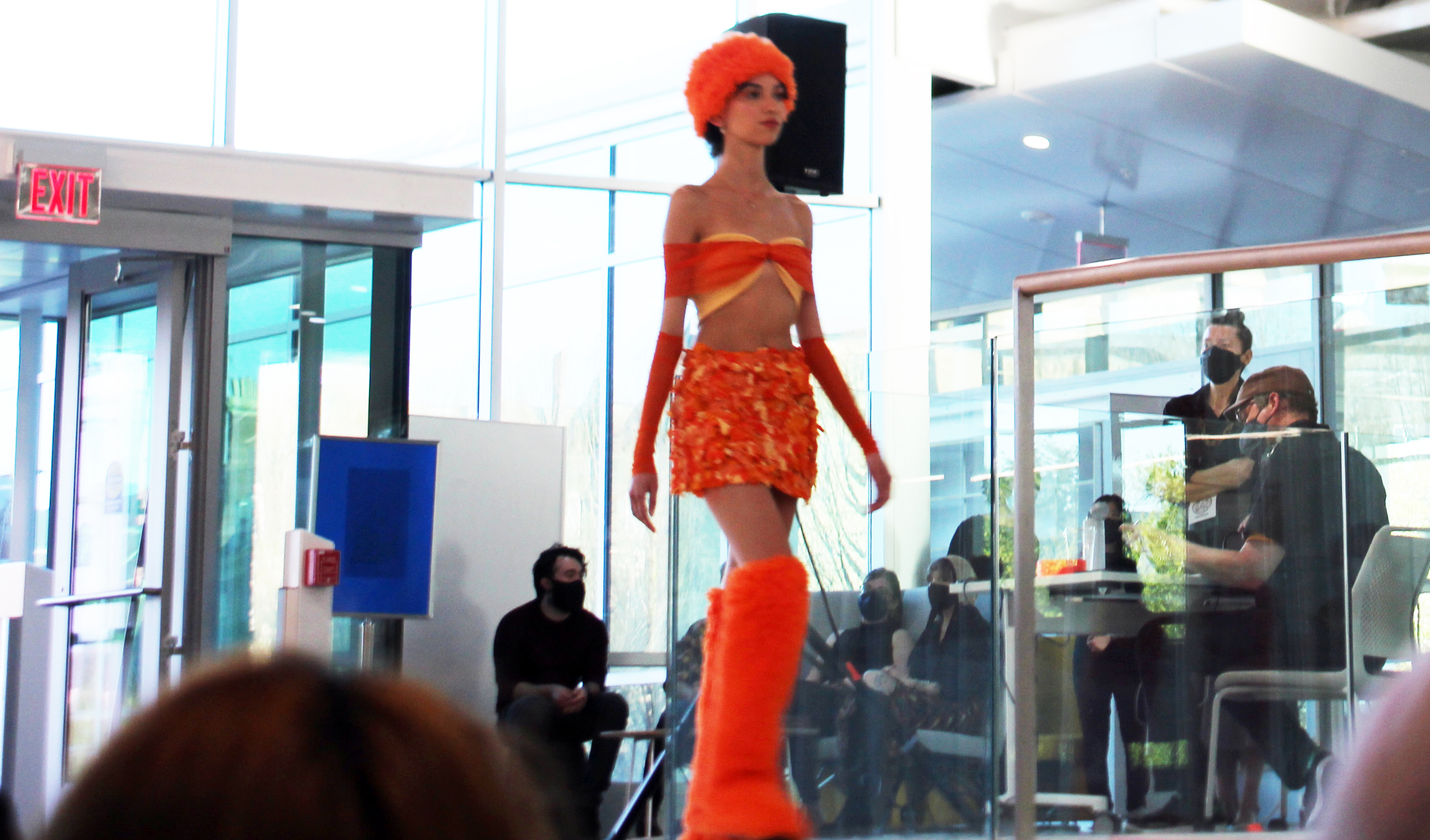 Female model in orange and yellow tube top and mini skirt with coordinating orange furry hat and boots.