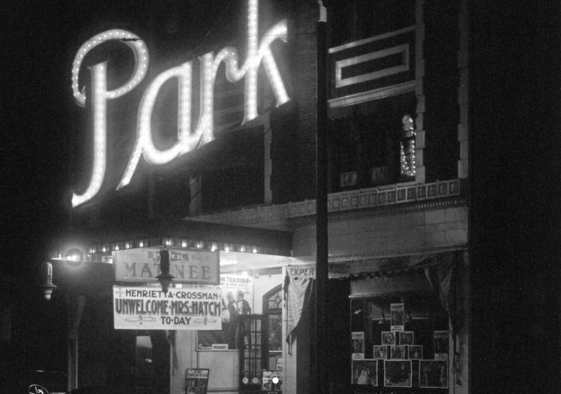 A black and white photo, probably from the 1920s through 1950s, of a theater with a large, well lit sign that says â€œPARK.â€ Below the large sign is a smaller, well lit marquee with a hanging banner that reads, â€œHarriet A. Crossman, Unwelcome Mrs. Match, Today.â€ Photo from the Champaign County History Museum Instagram page.