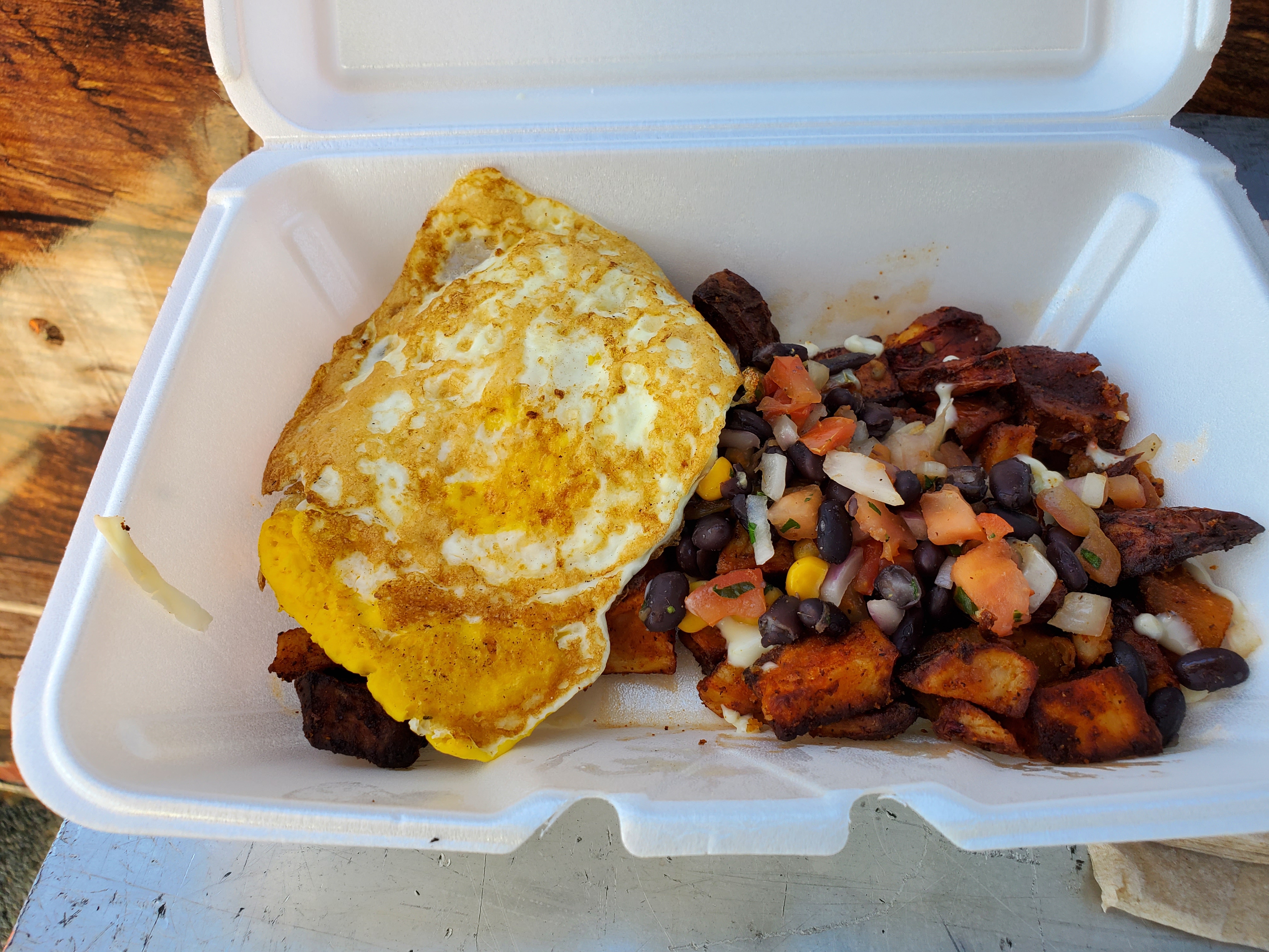In a white styrofoam container, there is a fried egg on top of sweet potato hash. Top image by Carl Busch.