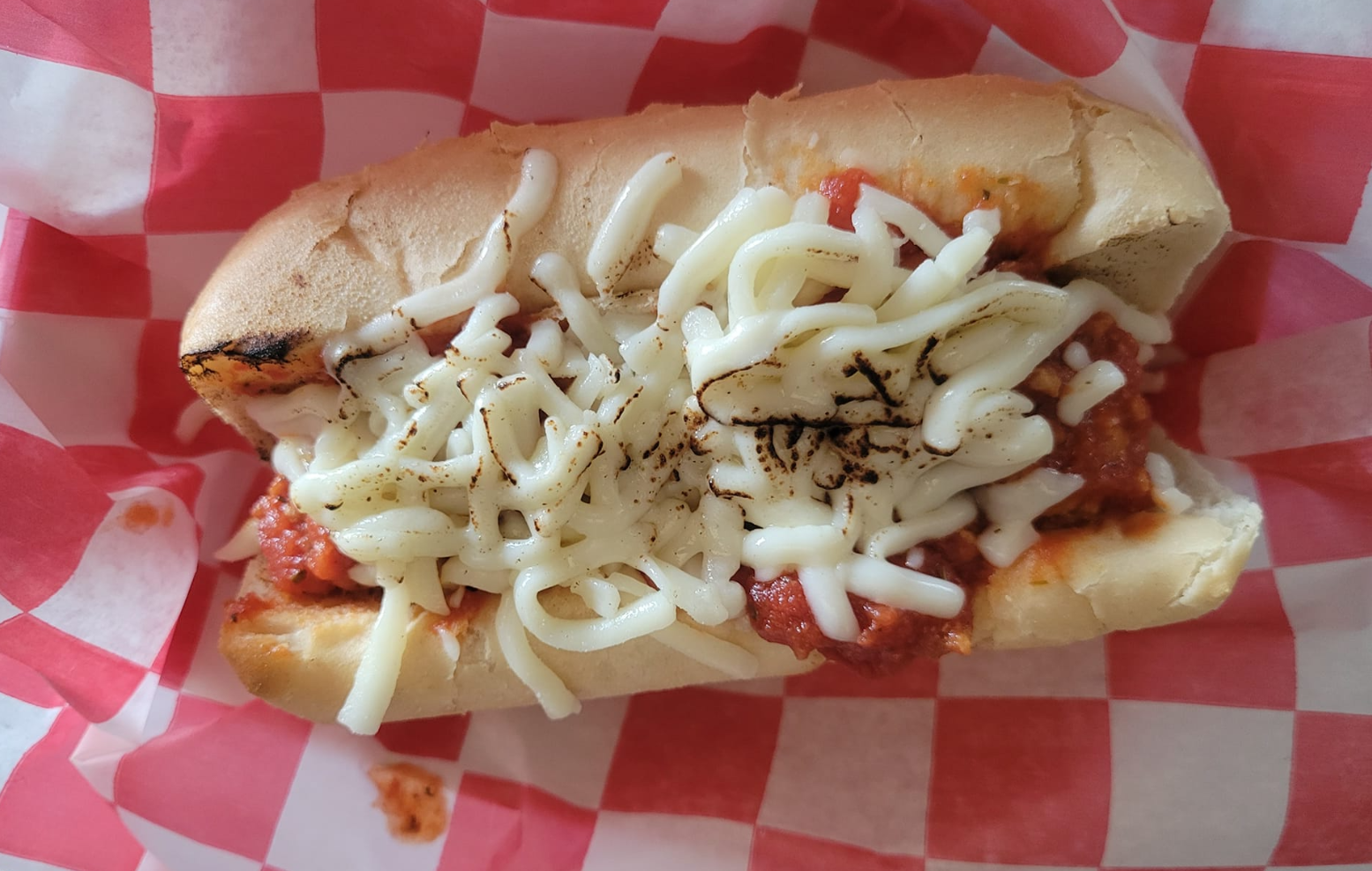 On red-and-white checkered parchment paper, there is a meatball sub in a hot dog bun covered in shredded cheese and spiced with black pepper. Photo from Brien's Bistro's Facebook page.