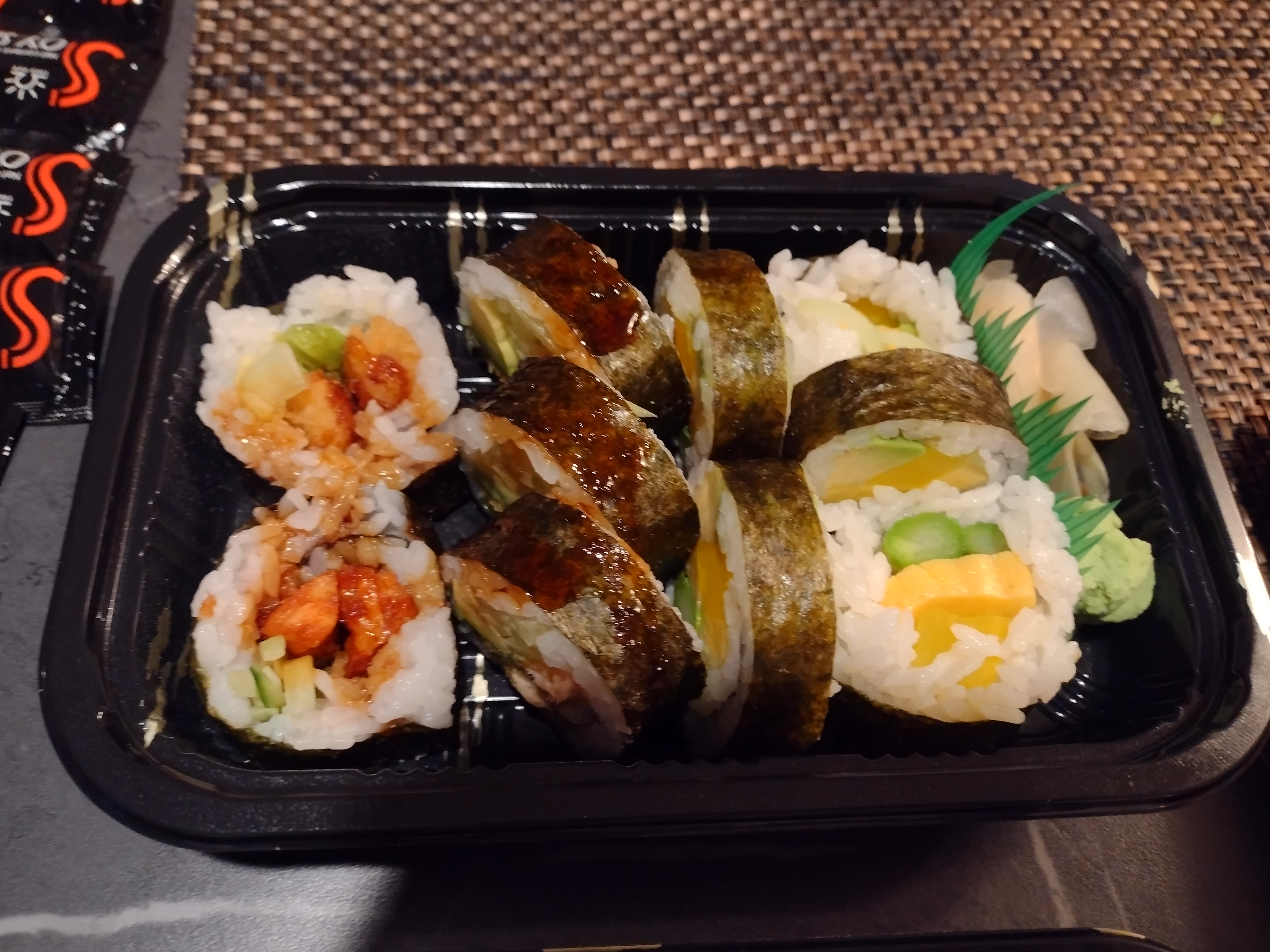 A salmon tempura roll and futomaki fill an entire black takeout container. Photo by Melkior Ornik.