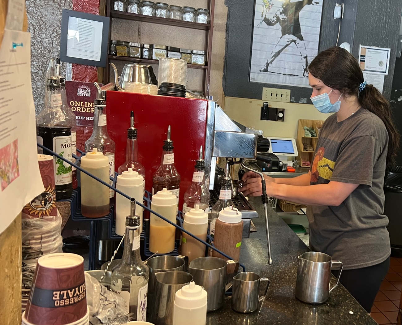 Manager Anika Nims makes a drink on the espresso machine at the Espresso Royale Krannert View location. She is masked in a blue mask and focused on the task. Photo by Alyssa Buckley.
