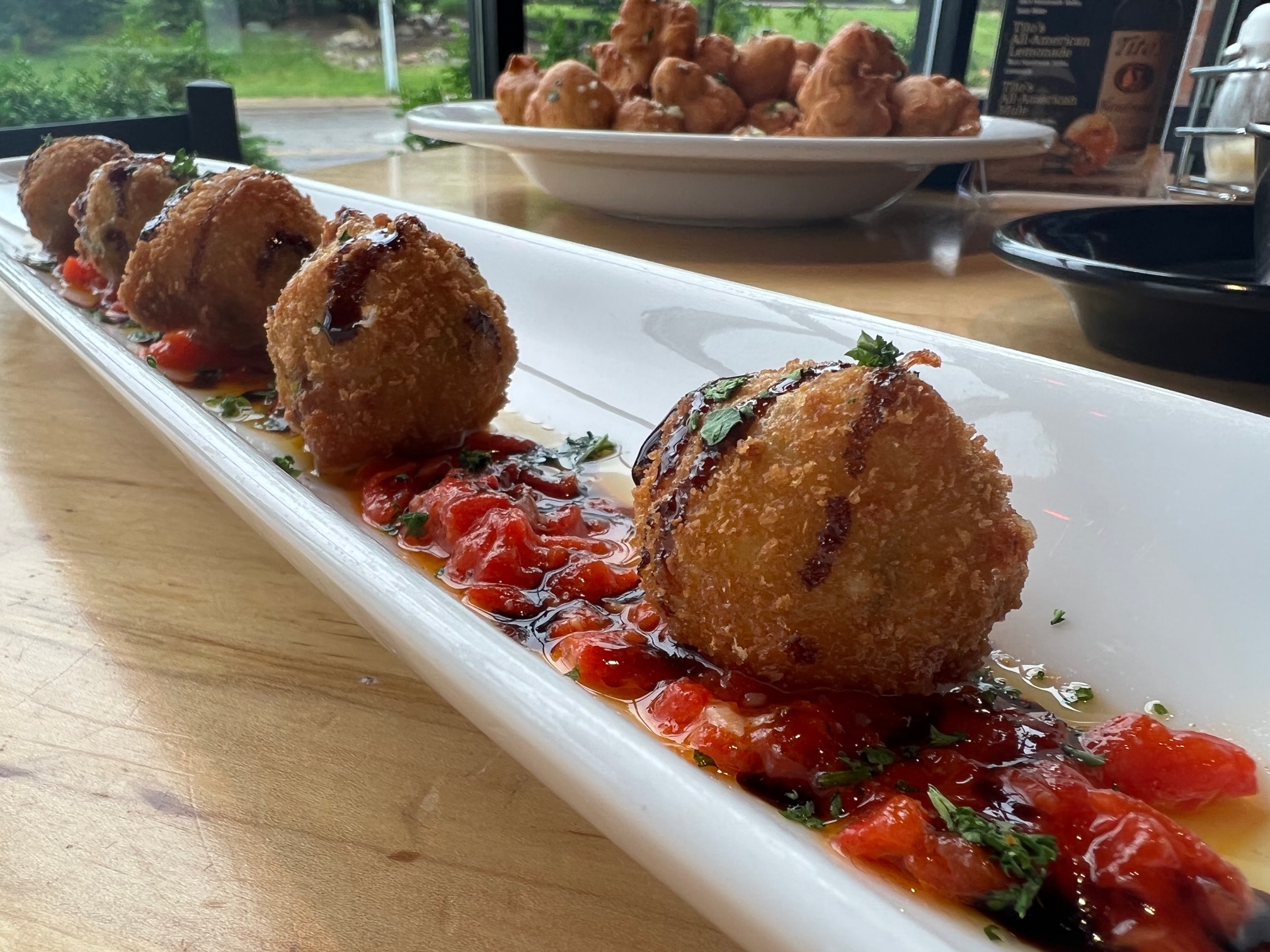 A close up of Papa Del's arancini. There are five panko breaded arancini on a long, skinny white plate. Photo by Alyssa Buckley.