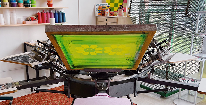 Photo of the inside of the screenprinting studio with paints and screens and screenprinting machinery.