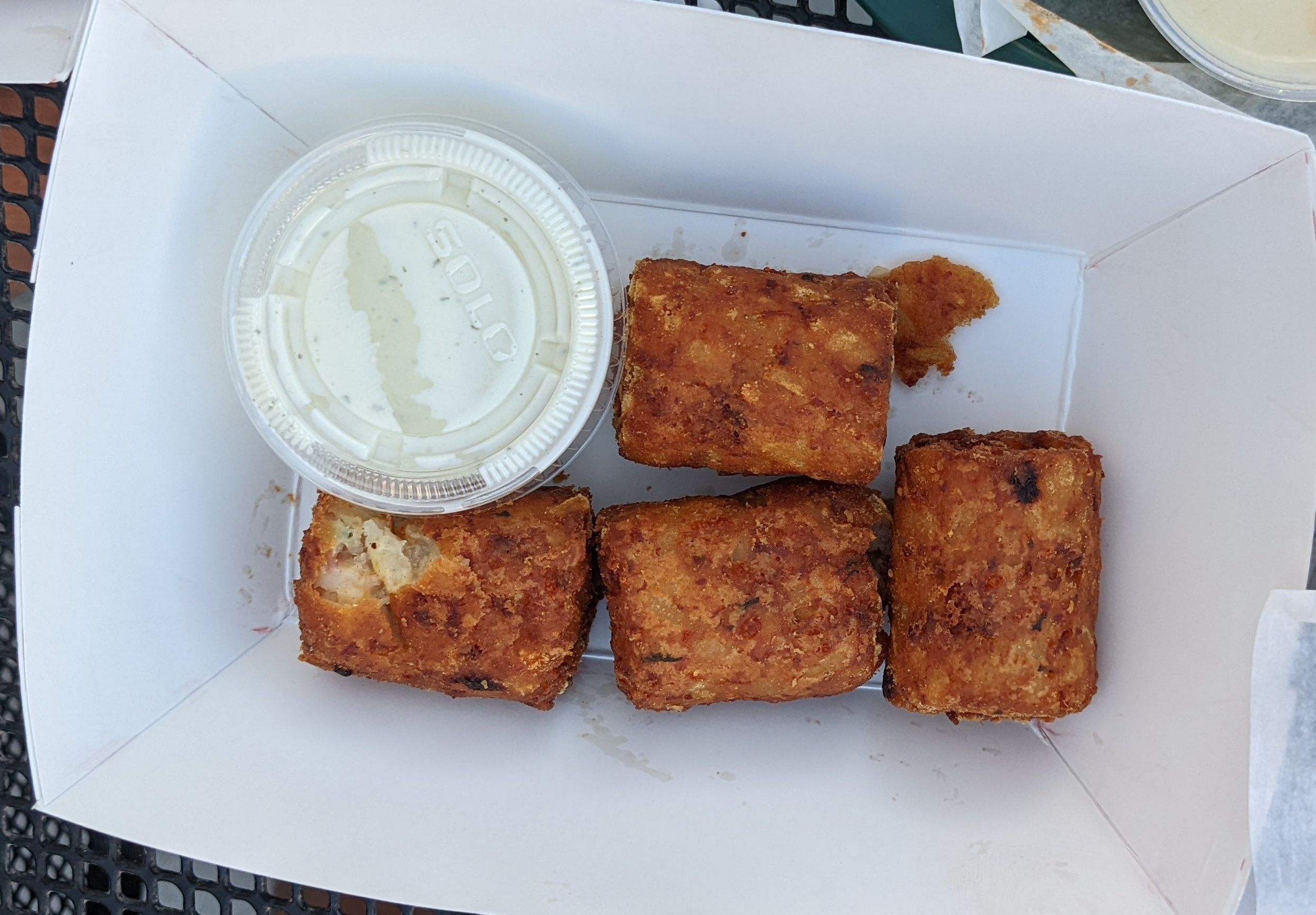 In a white paper basket, there are four giant tots with a cup of sauce. Photo by Tayler Neumann.