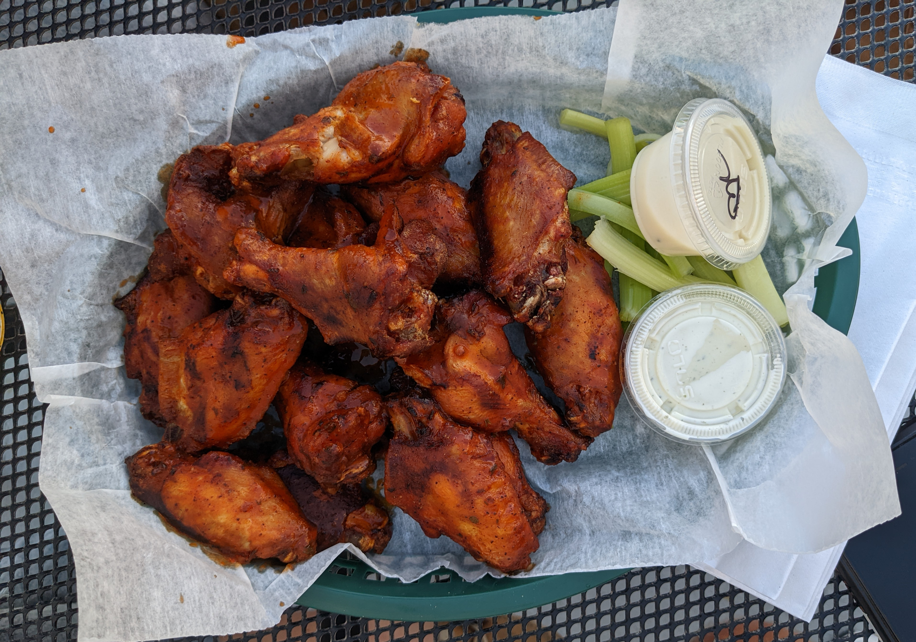 On a black outdoor table at Bunny's Tavern, there is a basket lined with parchment paper and full of chicken wings, celery, and a cup of ranch. Photo by Tayler Neumann.