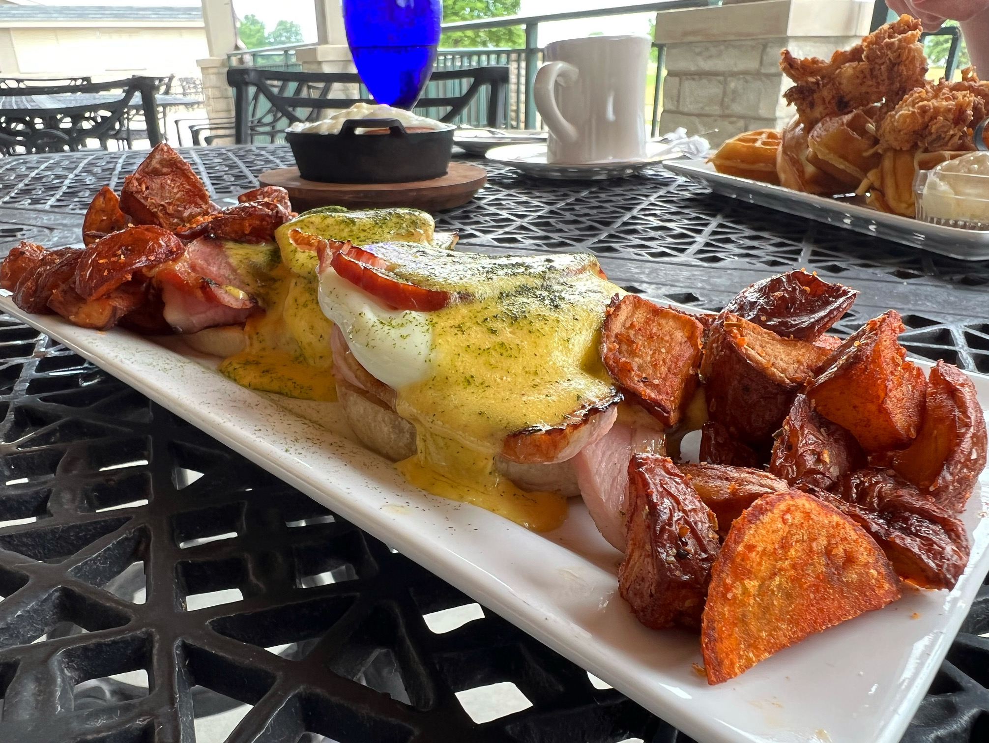 On a patio table, there is a white plate with eggs benedict and breakfast potatoes. Photo by Alyssa Buckley.