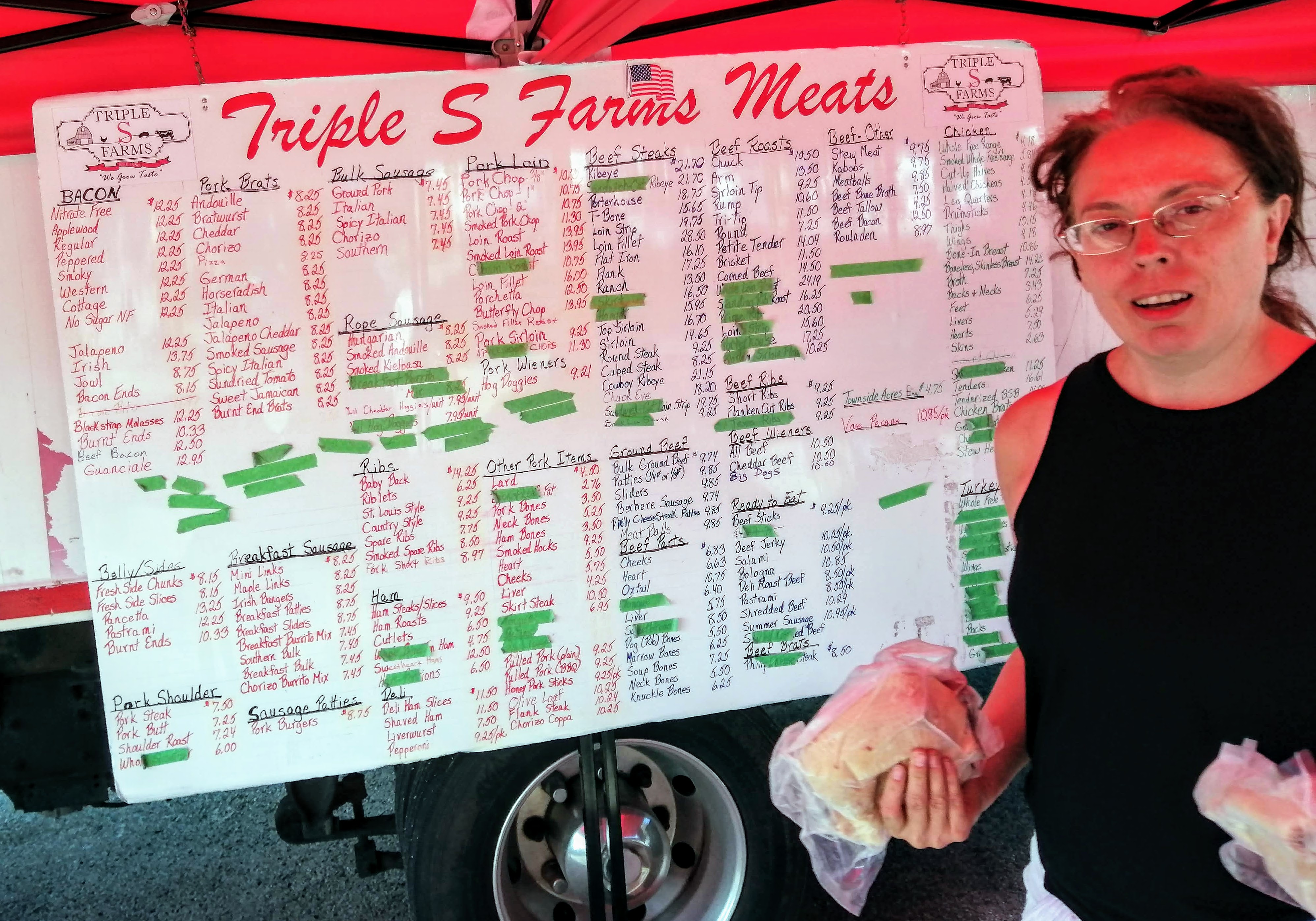 A woman holding two frozen packages of chicken in front of a very large hand-written menu board. Photo by Paul Young.