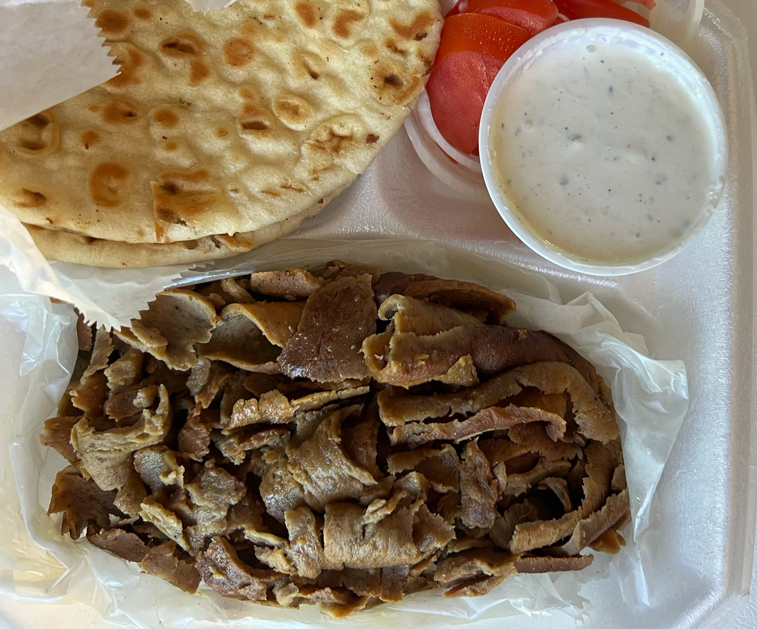 An overhead photo shows a half container of gyro meat with pitas blistered with brown spots, a few slices of tomato, and a few slices of white onion. Photo by Alyssa Buckley.