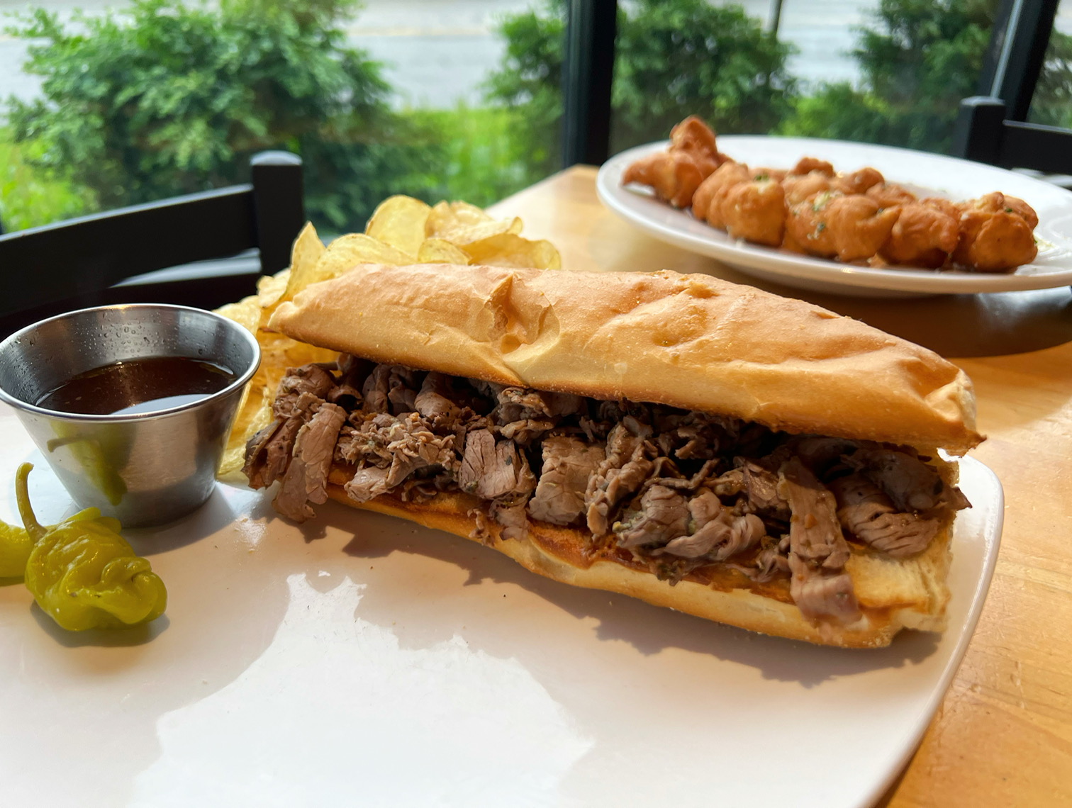 At Papa Del's in Champaign, there is an Italian beef sandwich on a white plate with a metal cup of dipping jus with peppers on the side. Photo by Alyssa Buckley.