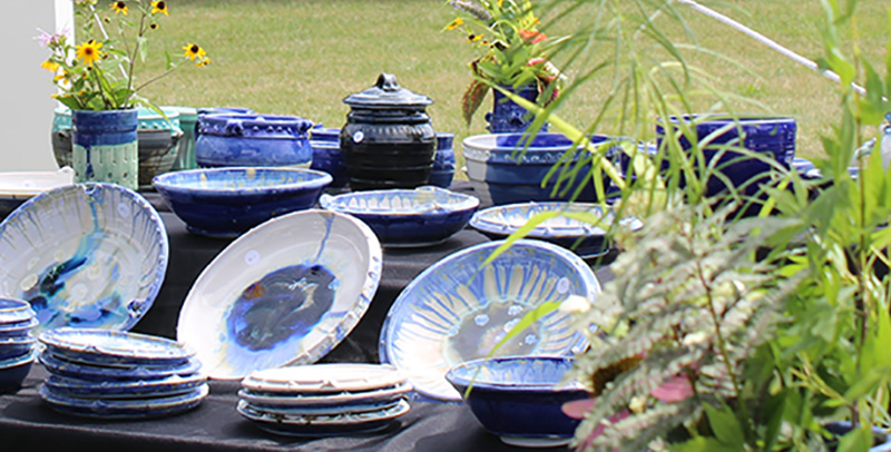 Display of blue-toned ceramics with plants and native flowers. 