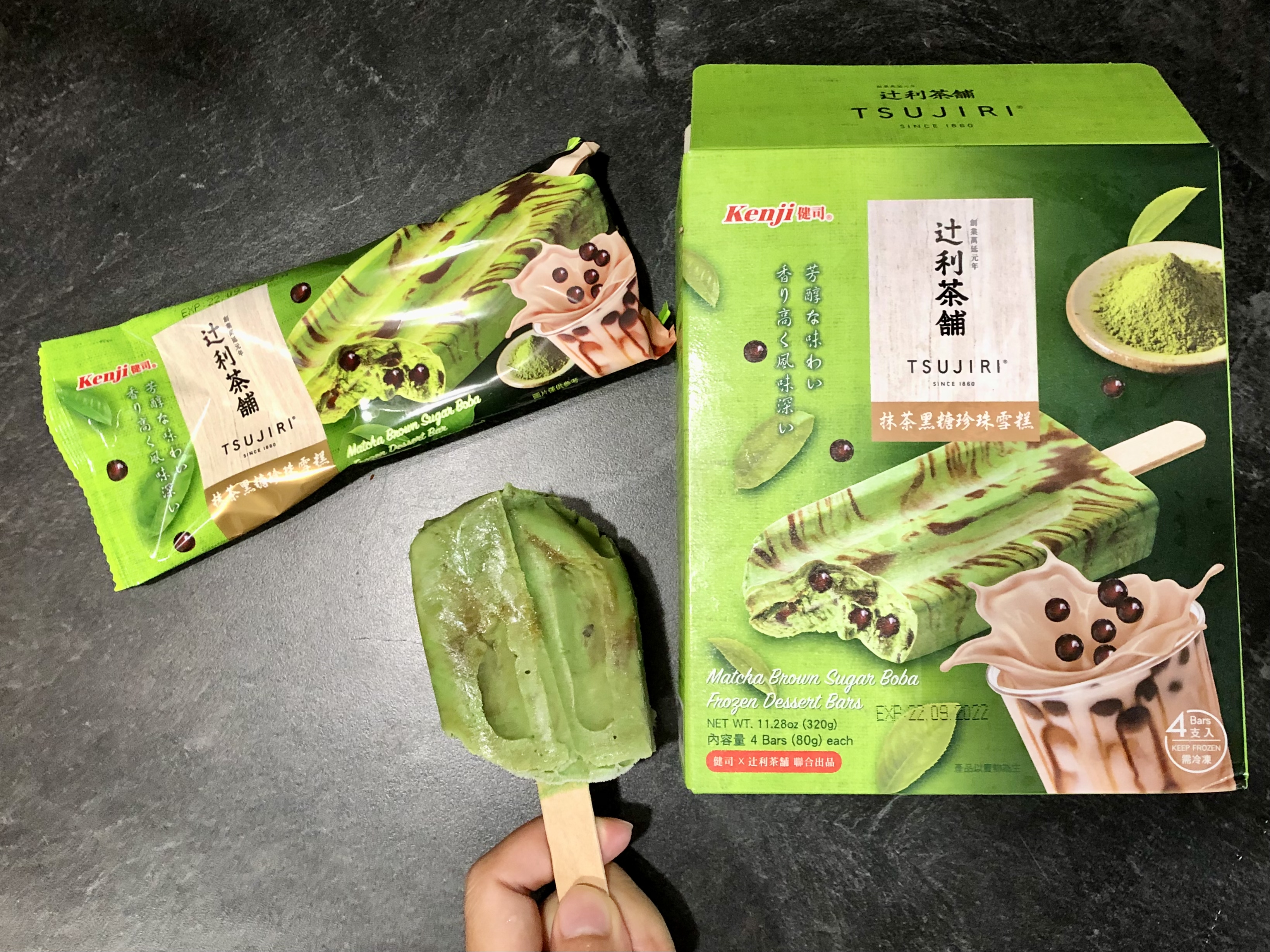 On a black counter, there is a green icepop with the green plastic packaging and matching paper box. Photo by Xiaohui Zhang.