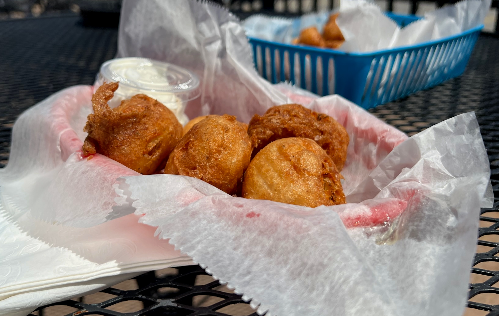 On a patio table on a sunny day, there is a parchment paper lined basket with huge fried, breaded balls of mashed potato. Photo by Alyssa Buckley.