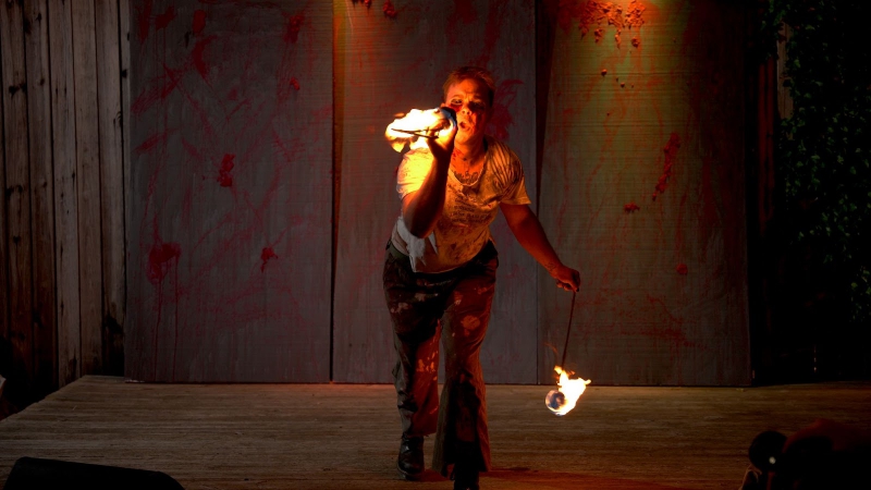 A performer in a white t shirt and black pants spattered with paint and blood is swinging two fire poi. Photo by Jeff Putney.