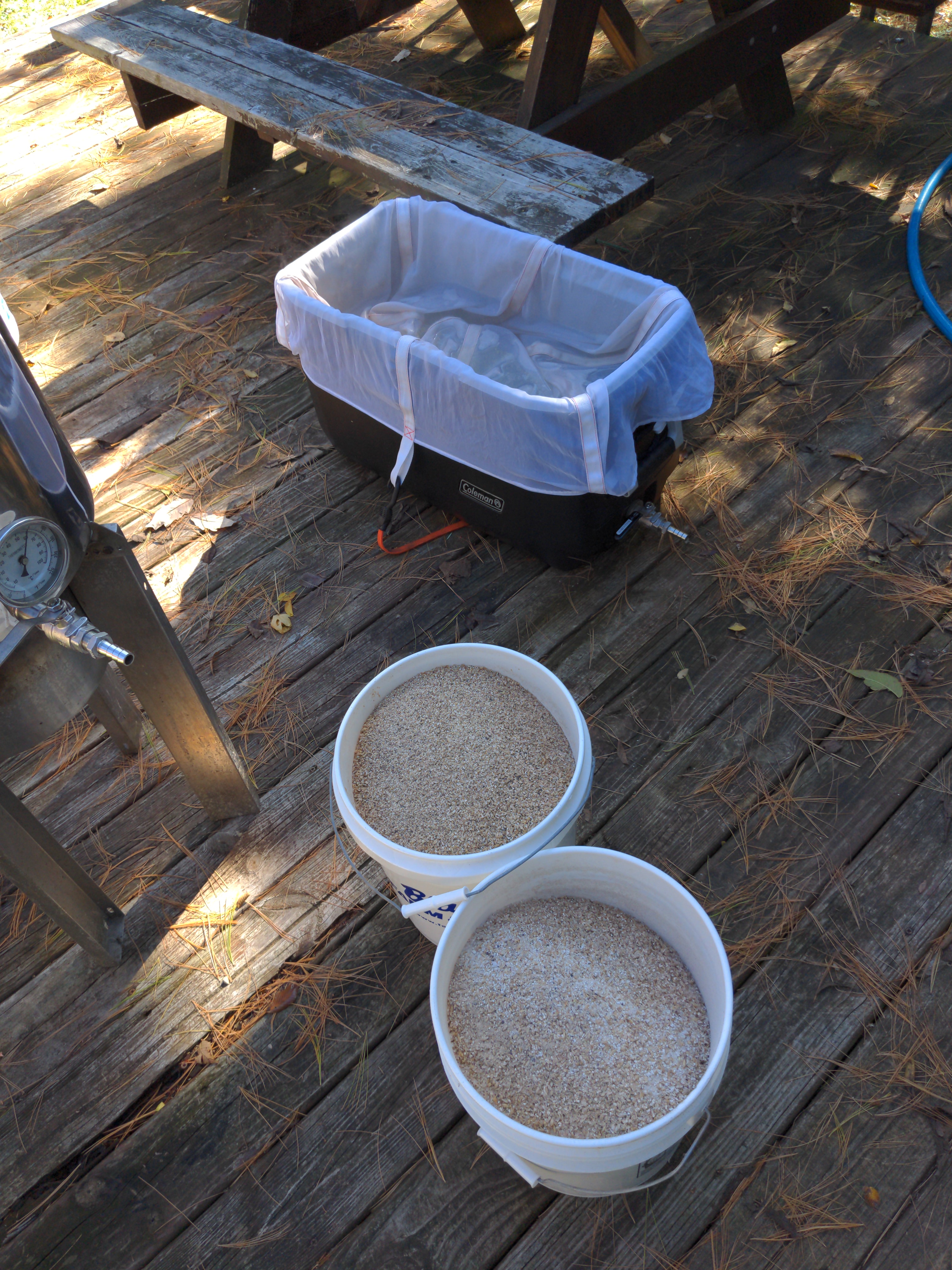 On a wooden deck, there is a simple homebrewing set up with a trashbag-lined cooler and two buckets of yeast. Photo by BUZZ Homebrew Club.