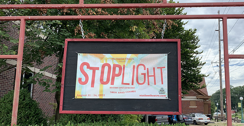 Photo of a horizontally oriented banner for the play Stoplight hanging outside of the Station Theatre in Urbana.
