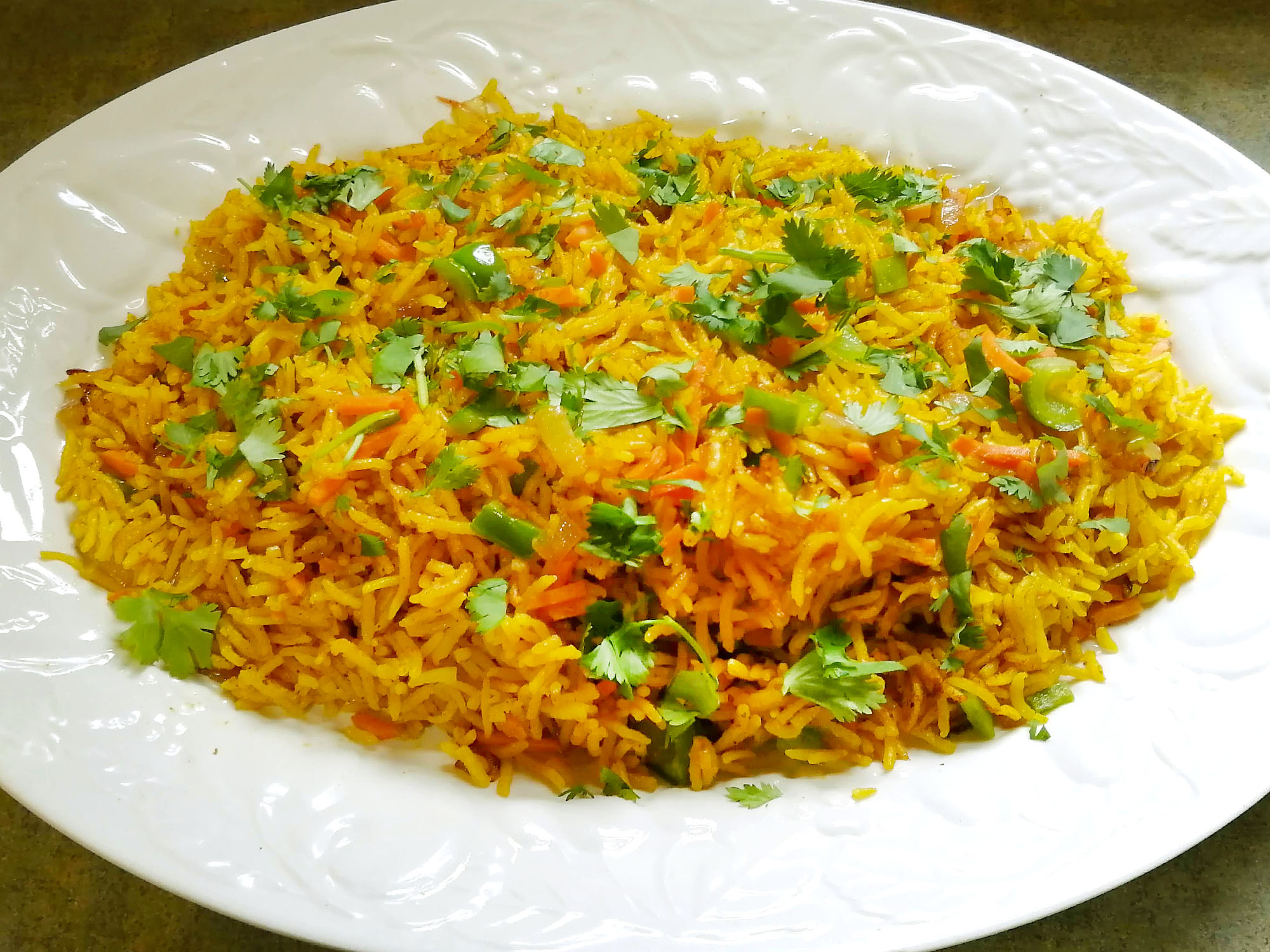 A large oval plate containing a yellowish rice dish called Biryani garnished with chopped cilantro leaves. Photo by Paul Young.