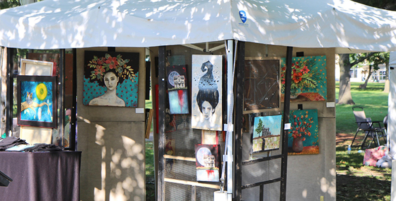 A large canvas tent filled with paintings of women's heads with whimsical designs in them.