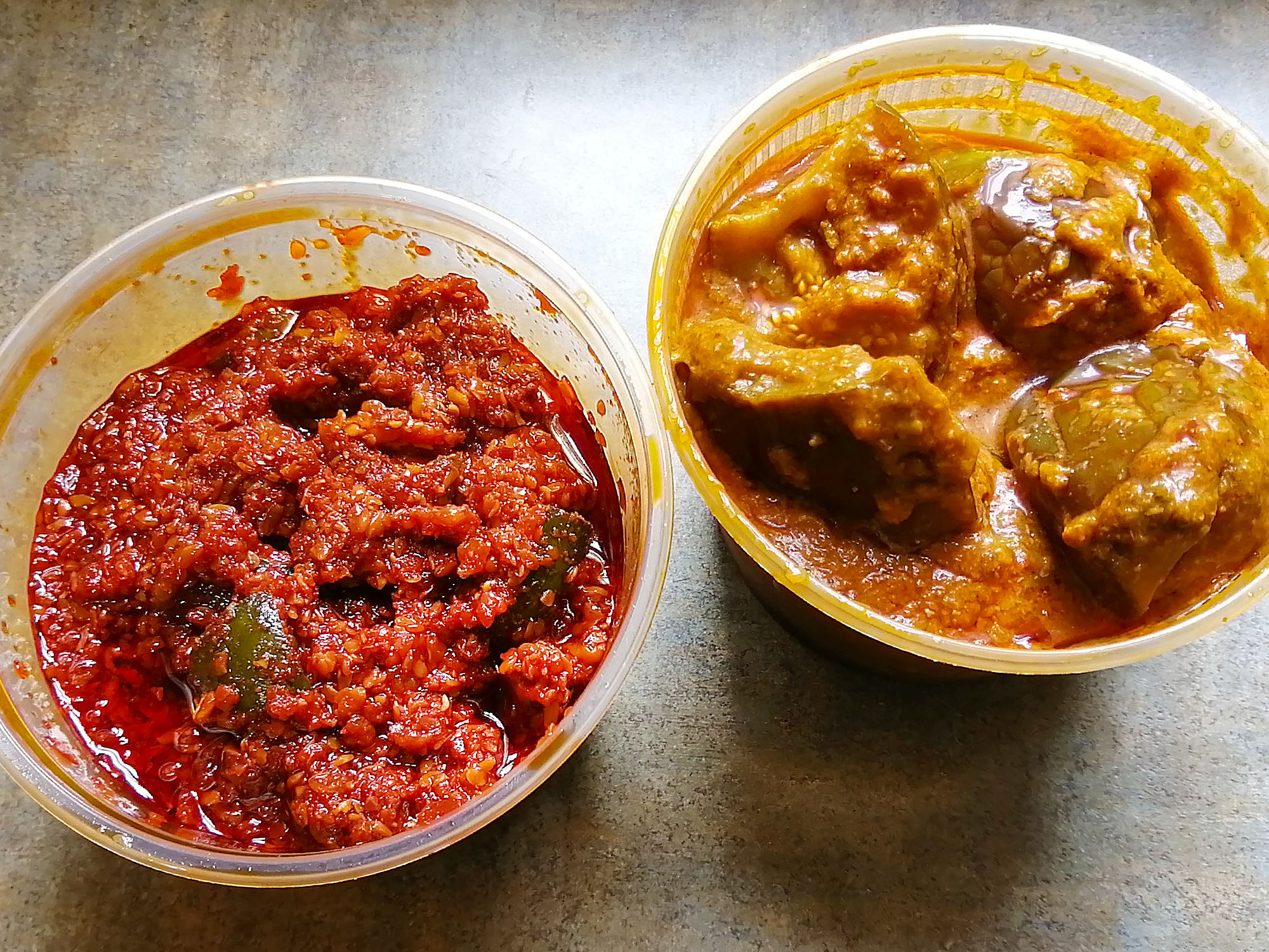 Two plastic to-go containers without lids revealing their contents; the left container has a reddish â€œmango pickleâ€ chutney in it, the right container has a yellowish â€œeggplant curryâ€ in it. Photo by Paul Young.