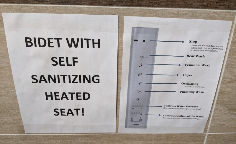Two signs hang side by side on a wall. One has instructions for the remote control, and the other says in black letters: Self Sanitizing Heated Seat! Photo by Tom Ackerman.