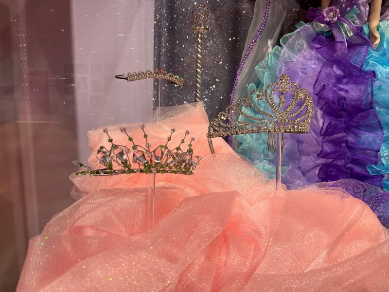 Three sparkly tiaras are on pedestals behind a pane of glass. They are surrounded by pink tulle. Photo by Julie McClure.